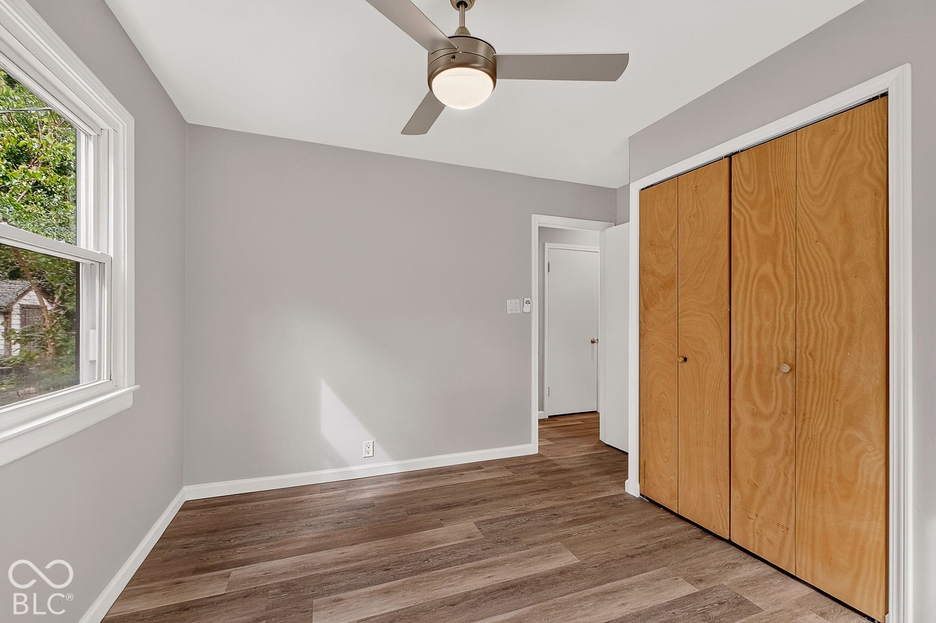 Wood-finish flooring, white trim, light gray walls, built-in closet with wood-grain doors, and a ceiling fan with integrated lighting