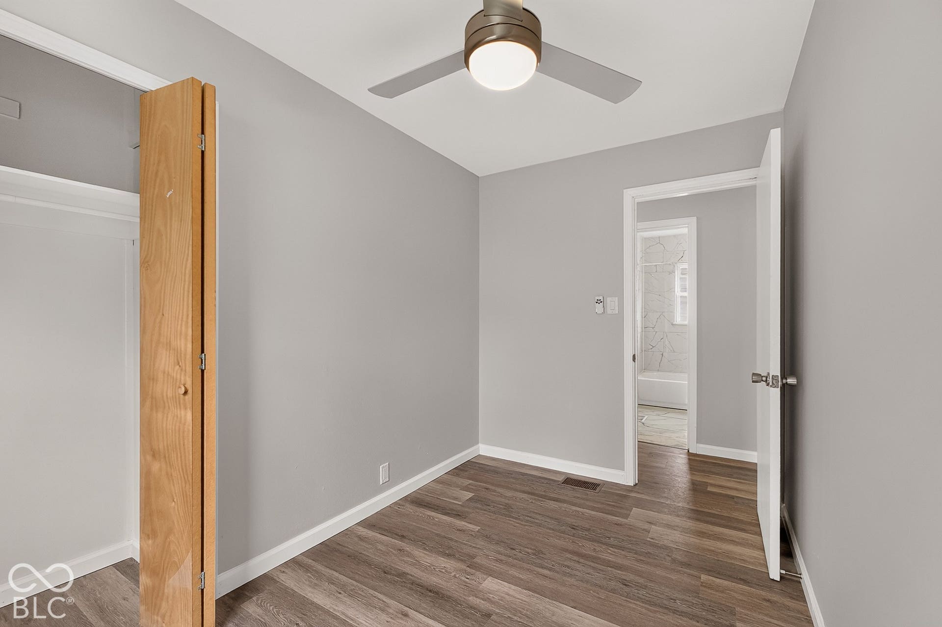 Wood-finish flooring, light grey wall paint, and a ceiling fan with integrated lighting