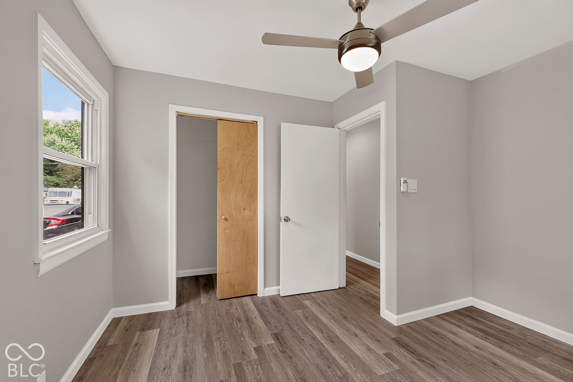 Wood-finish flooring, neutral gray wall tones, and a ceiling fan with integrated lighting