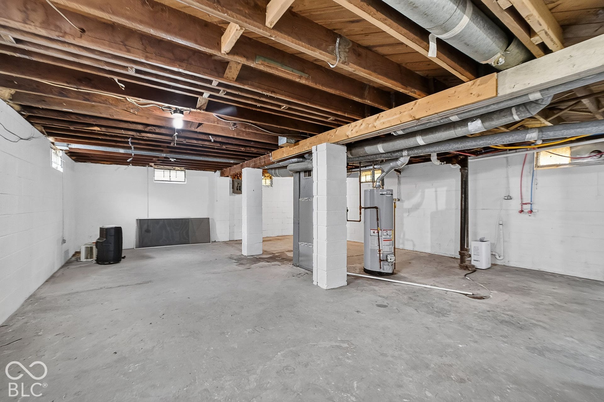Open floor plan with concrete flooring, exposed wood beam ceiling, and a water heater