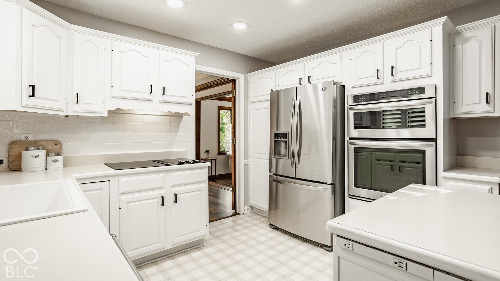 White cabinetry with black hardware, integrated stainless steel appliances, convection oven, a flush-mount electric cooktop, new LED recessed lighting and doors to dining room.