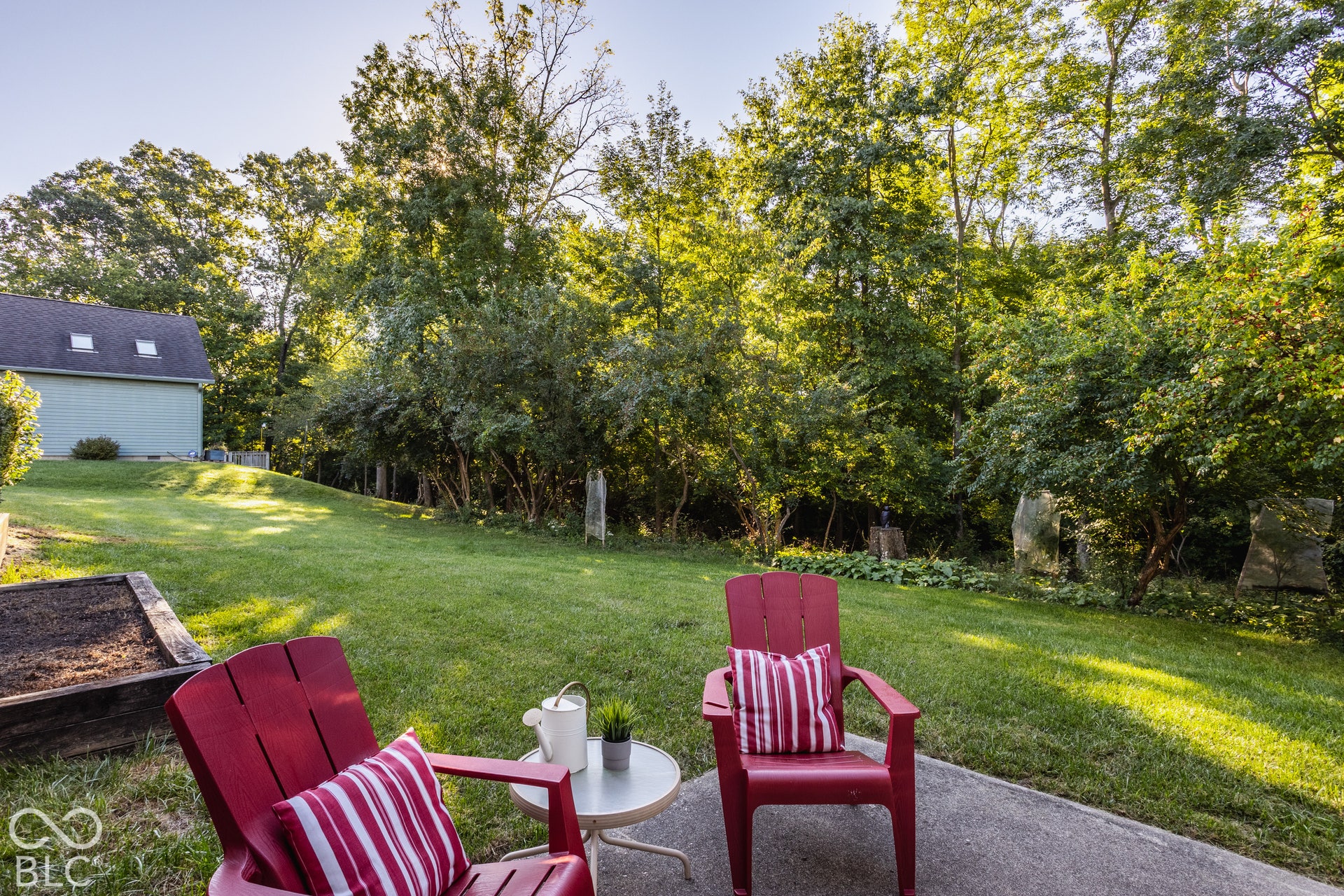 Back yard with expansive grassy lawn and a concrete patio by the walk out basement with fruit trees and private woods.