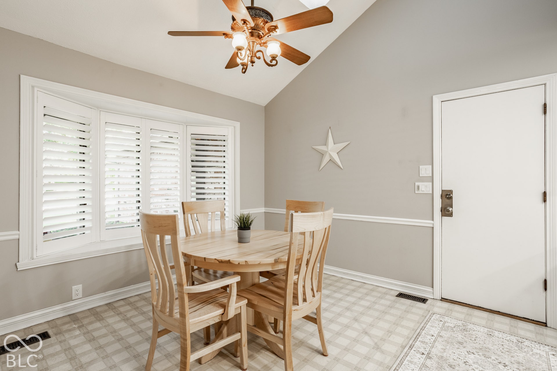 Eat in kitchen with vaulted ceiling, bay window with plantation shutters, ceiling fan with integrated lighting, wall molding, and neutral wall paint