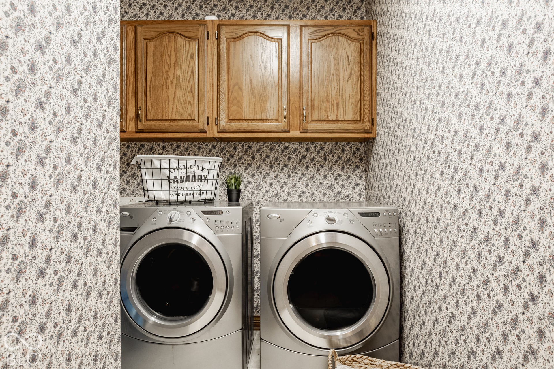 Wood-finish cabinetry, patterned wallpaper, and built-in laundry appliances