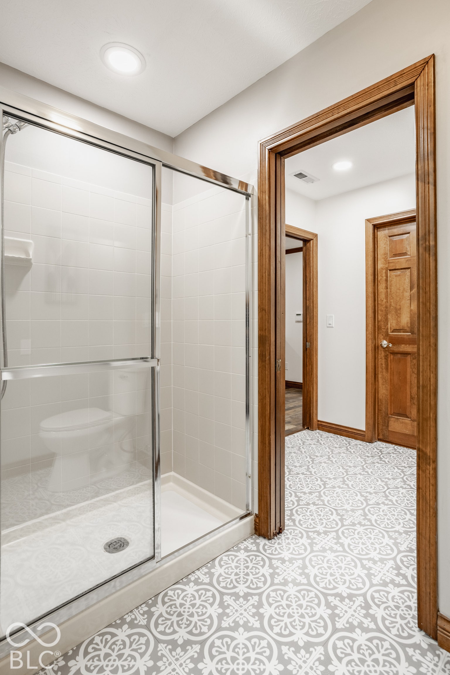 Stand alone shower with sliding glass door, white tile surround, and door leading to dual vanity.