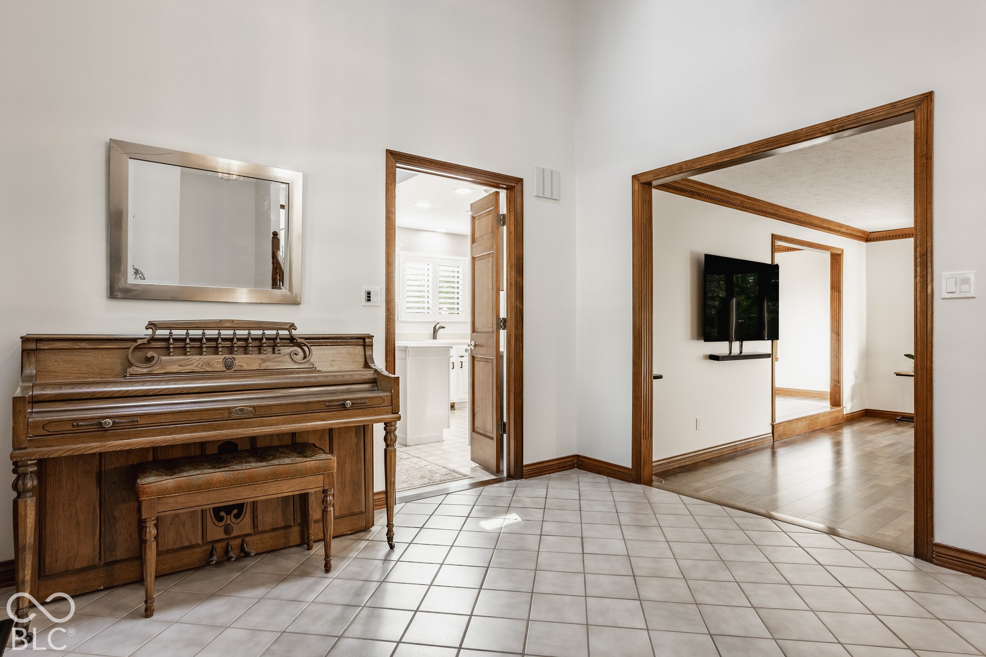 White tiled flooring, light wood-finish trim, and fresh white paint in foyer with vaulted ceiling leading to step down living room and eat in kitchen.