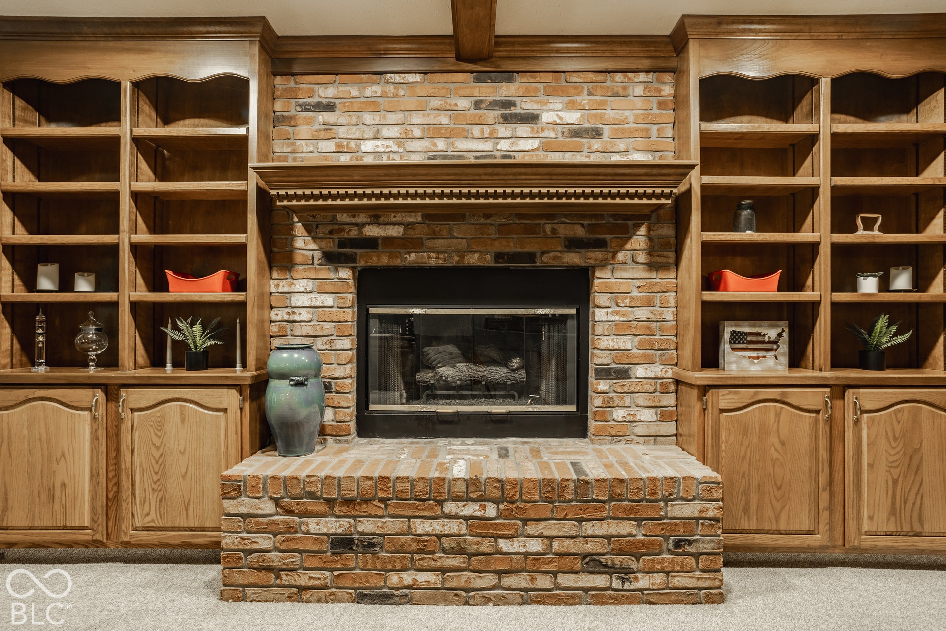 Brick fireplace with a substantial hearth, flanked by built-in wood cabinetry, integrated shelving, and a detailed wood mantelpiece