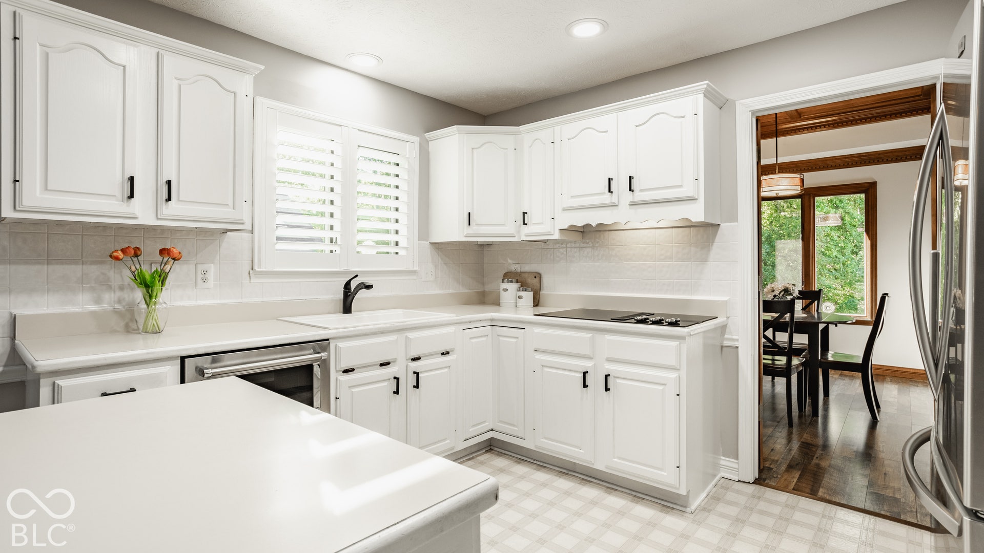 Kitchen with integrated white kitchen sink, built-in flat electric cooktop, and window with plantation shutters
