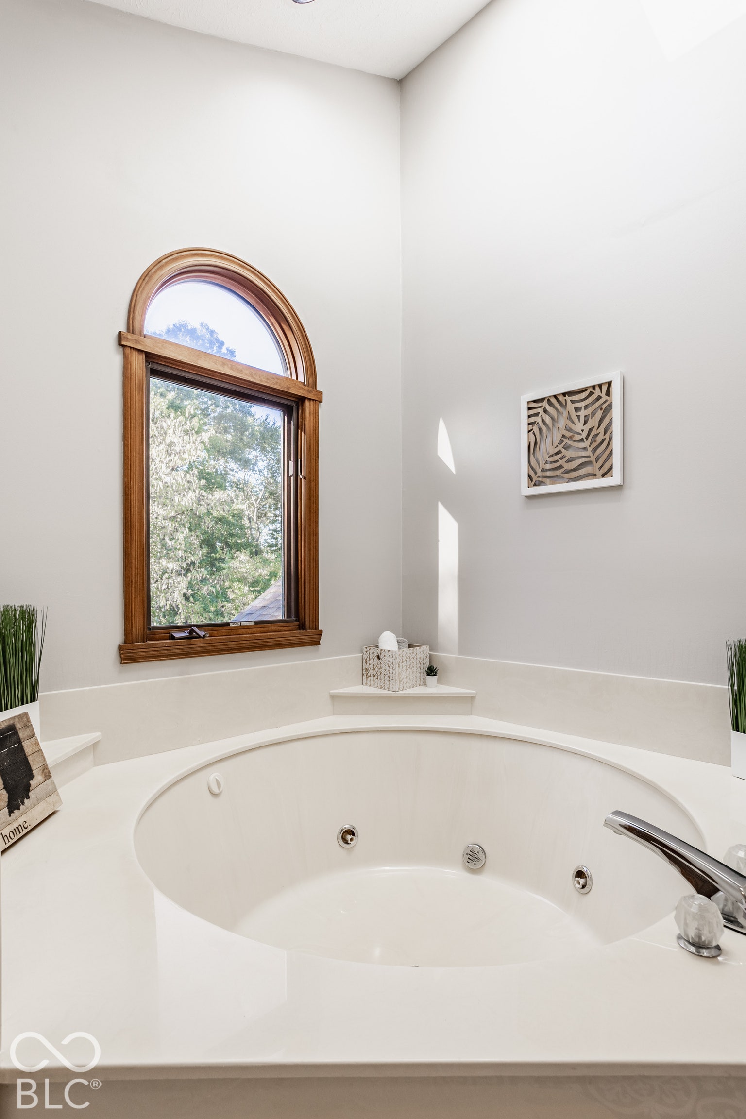 Built-in jetted tub with light-colored surfacing and integrated faucet fixtures, set beneath a large arched window with wood framing