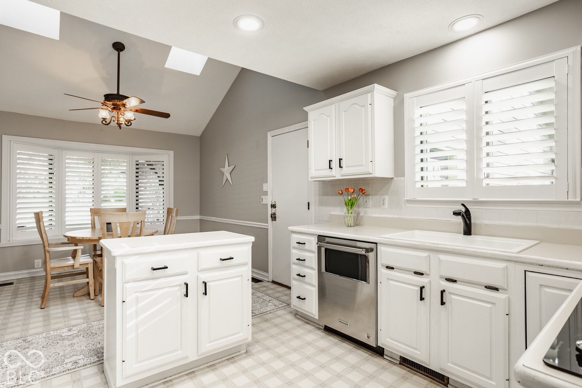 Kitchen featuring white cabinetry, stainless steel dishwasher, white sink with matte black faucet, custom plantation shutters and new skylights.