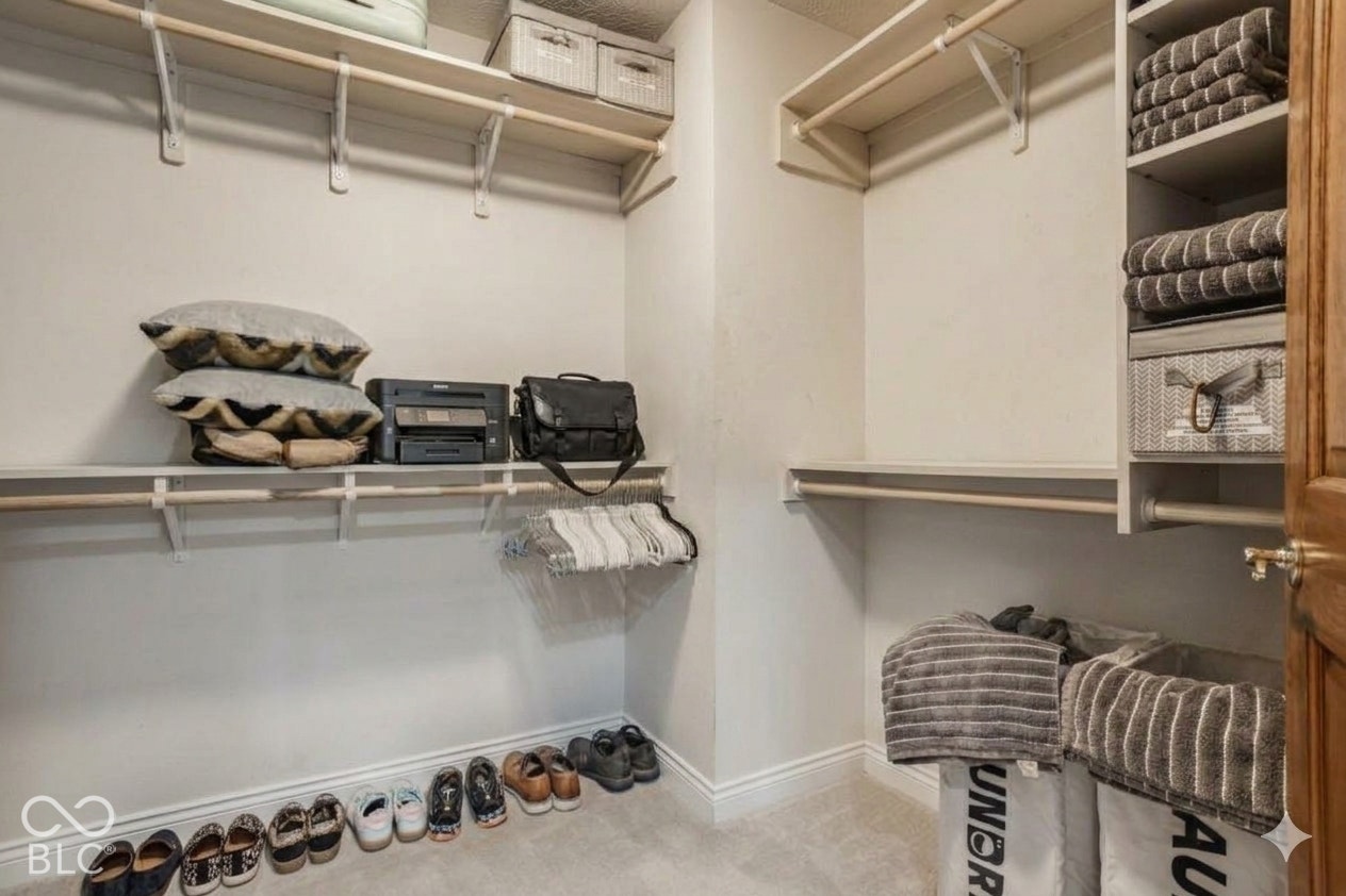 Virtually Altered - Primary suite with Built-in closet shelving and hanging rods with a carpeted floor. Virtually altered: belongings removed.