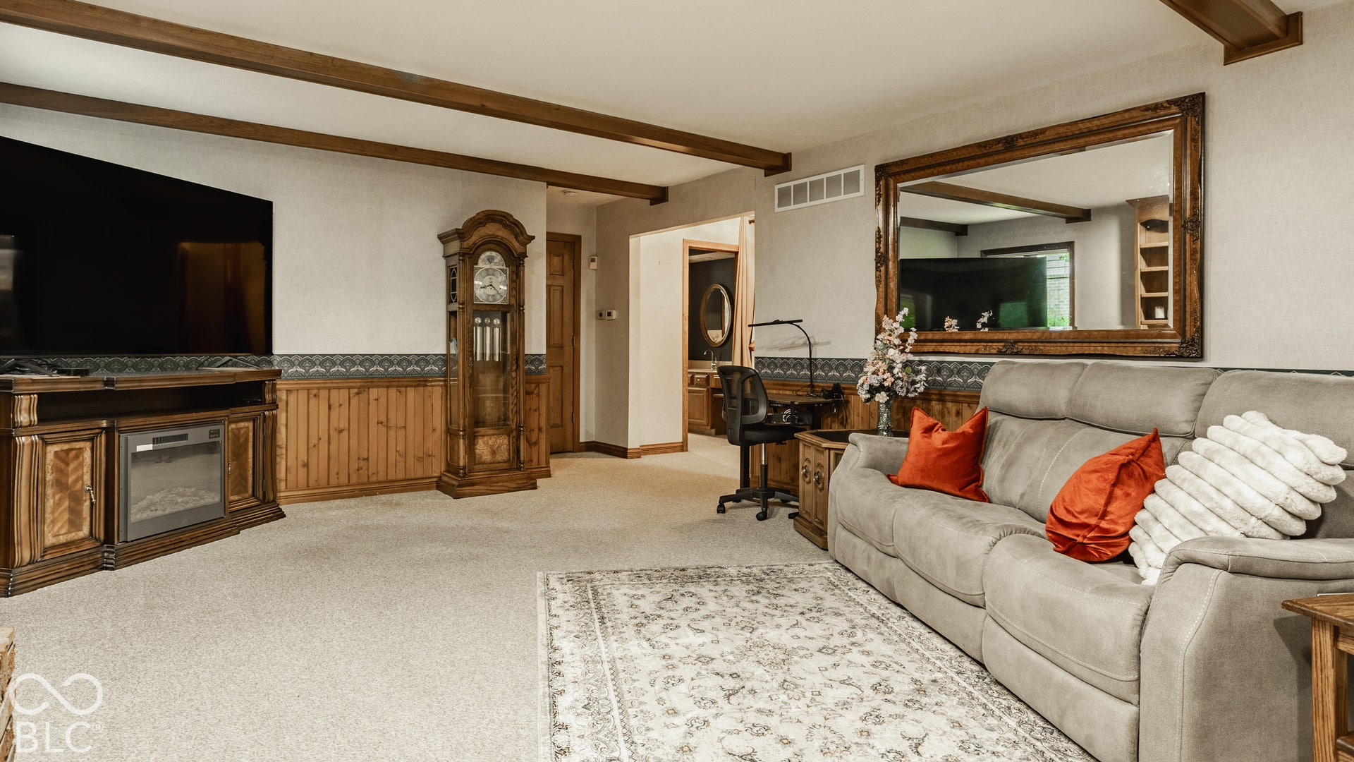 Basement apartment with faux wood beams, carpeted flooring, and wood-paneled wall accents