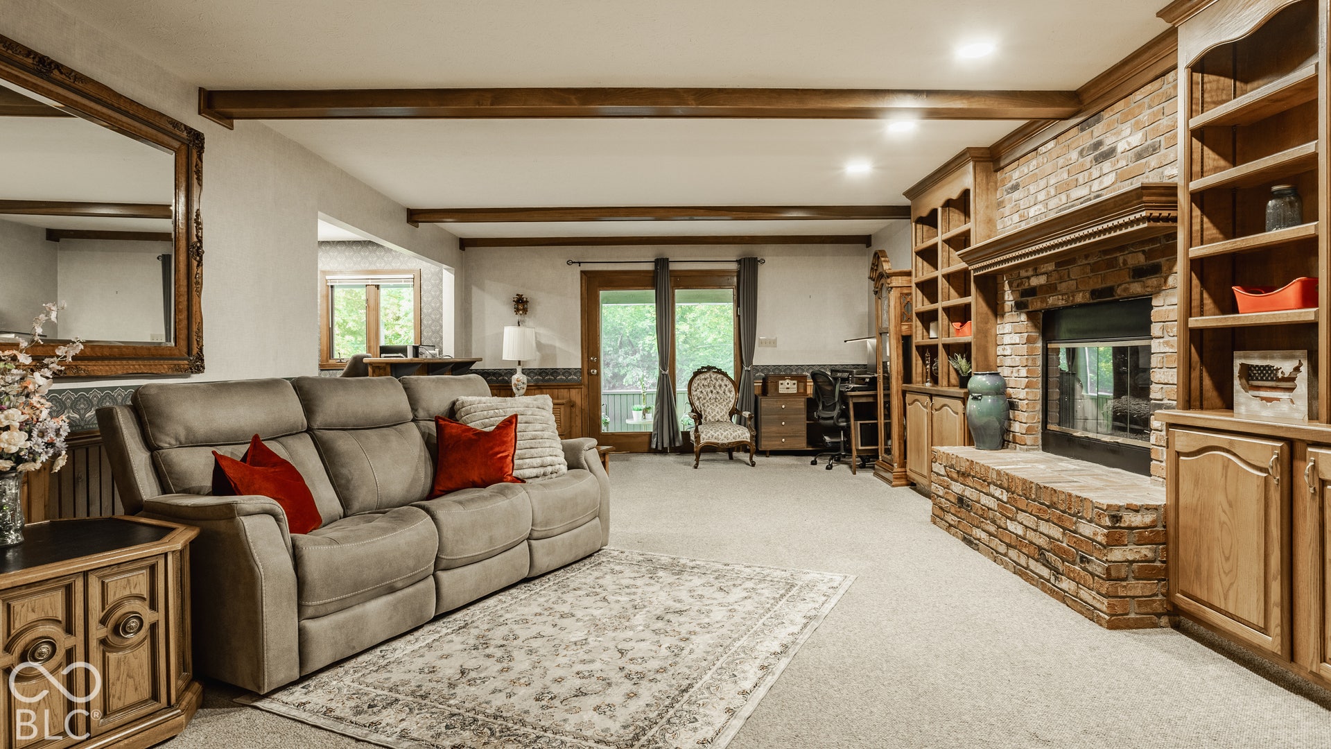 Brick fireplace with hearth, built-in shelving, wood-finish ceiling beams, and a sliding glass door that leads to the screened porch.