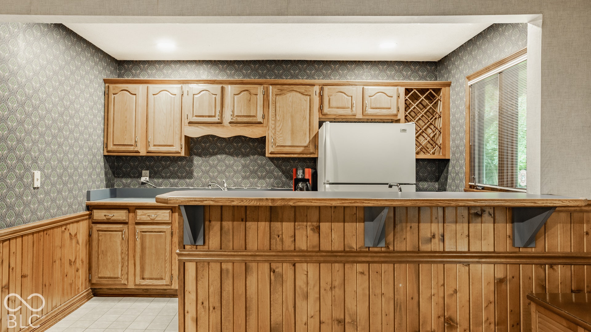 Built-in bar featuring wood paneling, upper and lower cabinetry, a wine rack, and full sized fridge.