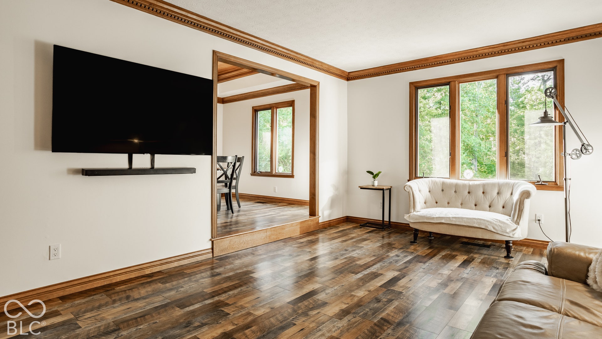 Step down living room with wooded views, new LVP flooring throughout, framed by natural wood trim and crown molding