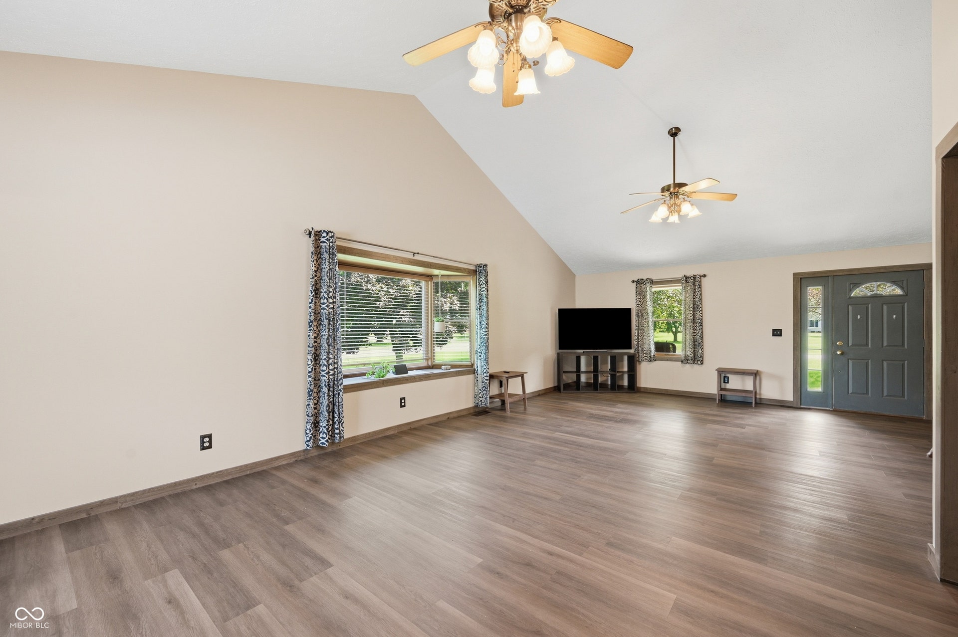 Vaulted ceiling with dual ceiling fans, wood-finish flooring, bay window with integrated sill, and a paneled entry door with transom window