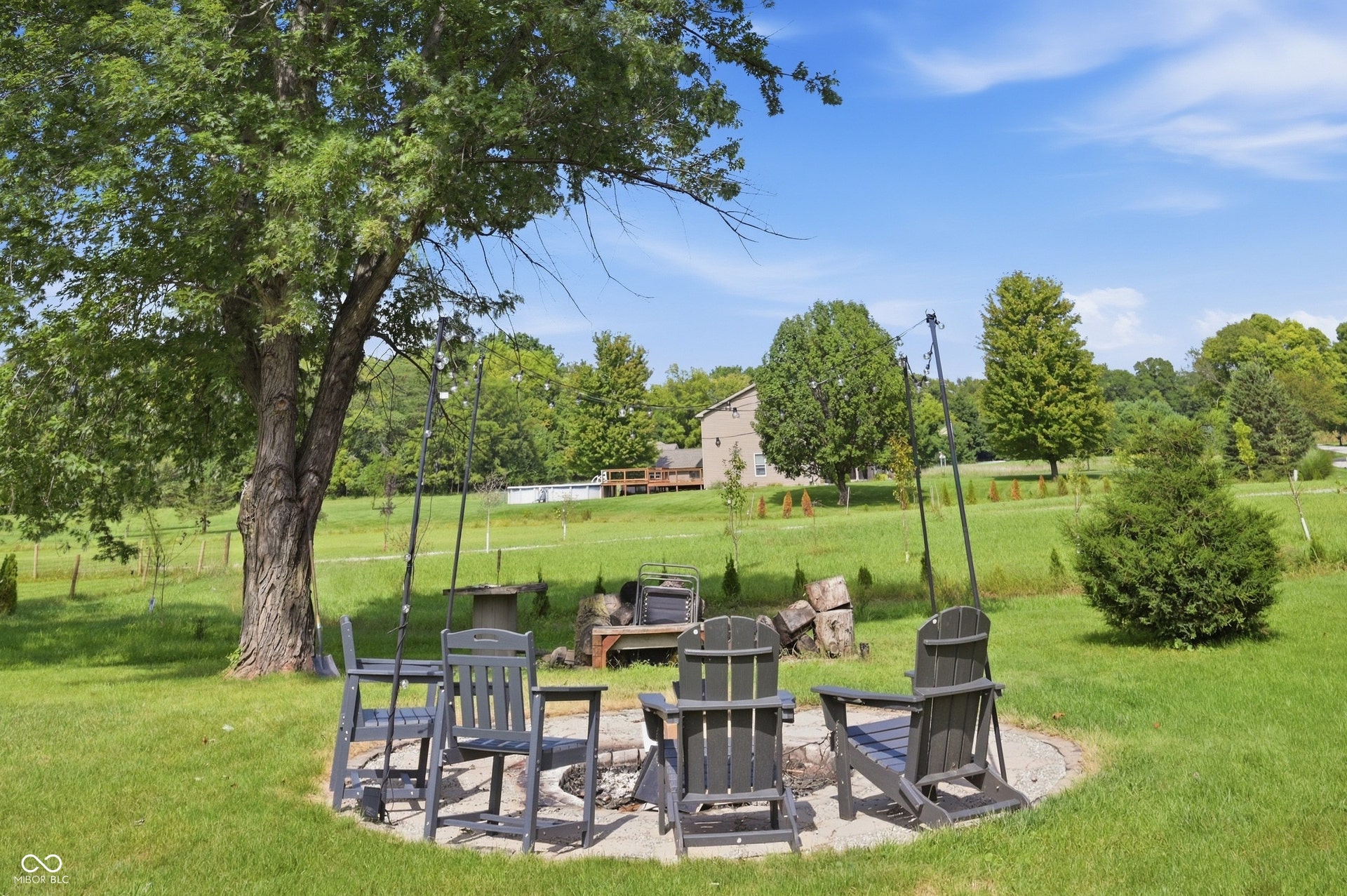 Expansive green space featuring a mature tree, a stone fire pit, and scattered trees