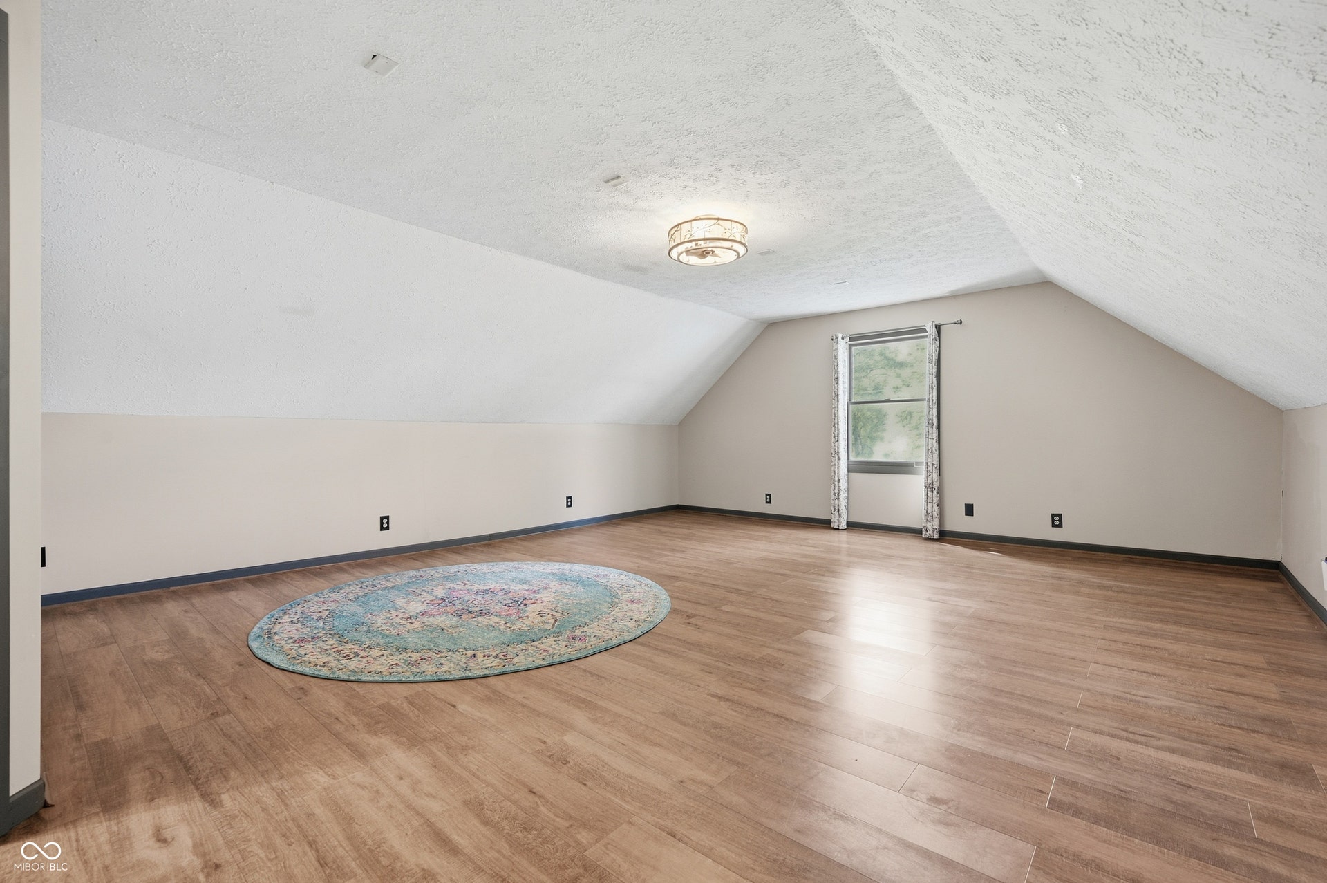 Spacious room featuring vaulted ceilings, wood-finish flooring, a contemporary ceiling light fixture, and a window with natural light