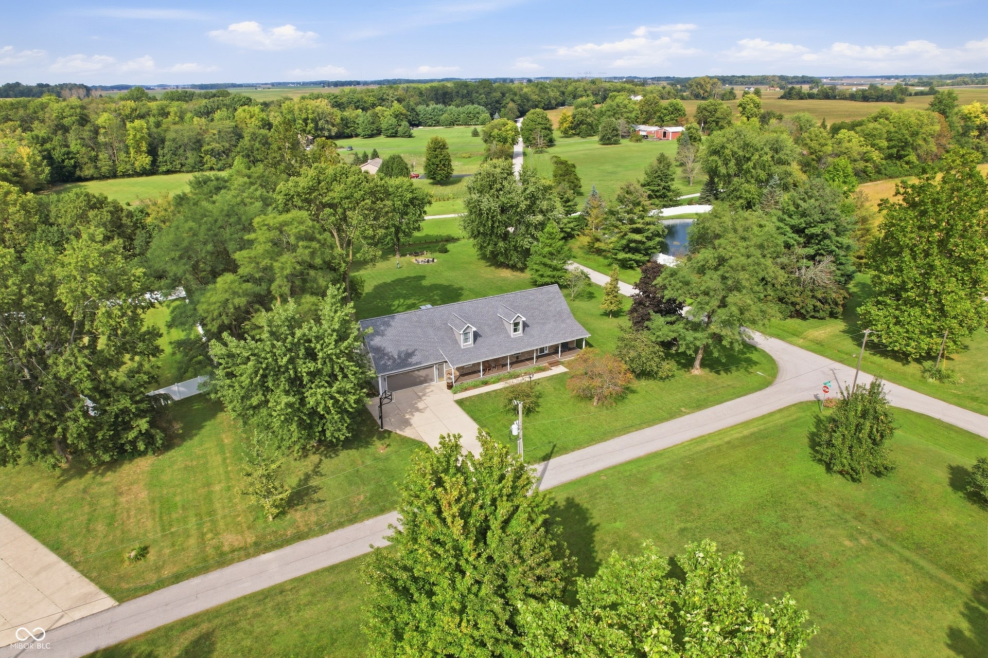 Spacious property featuring a single-story residence with a gray shingle roof, attached garage, and a covered front porch
