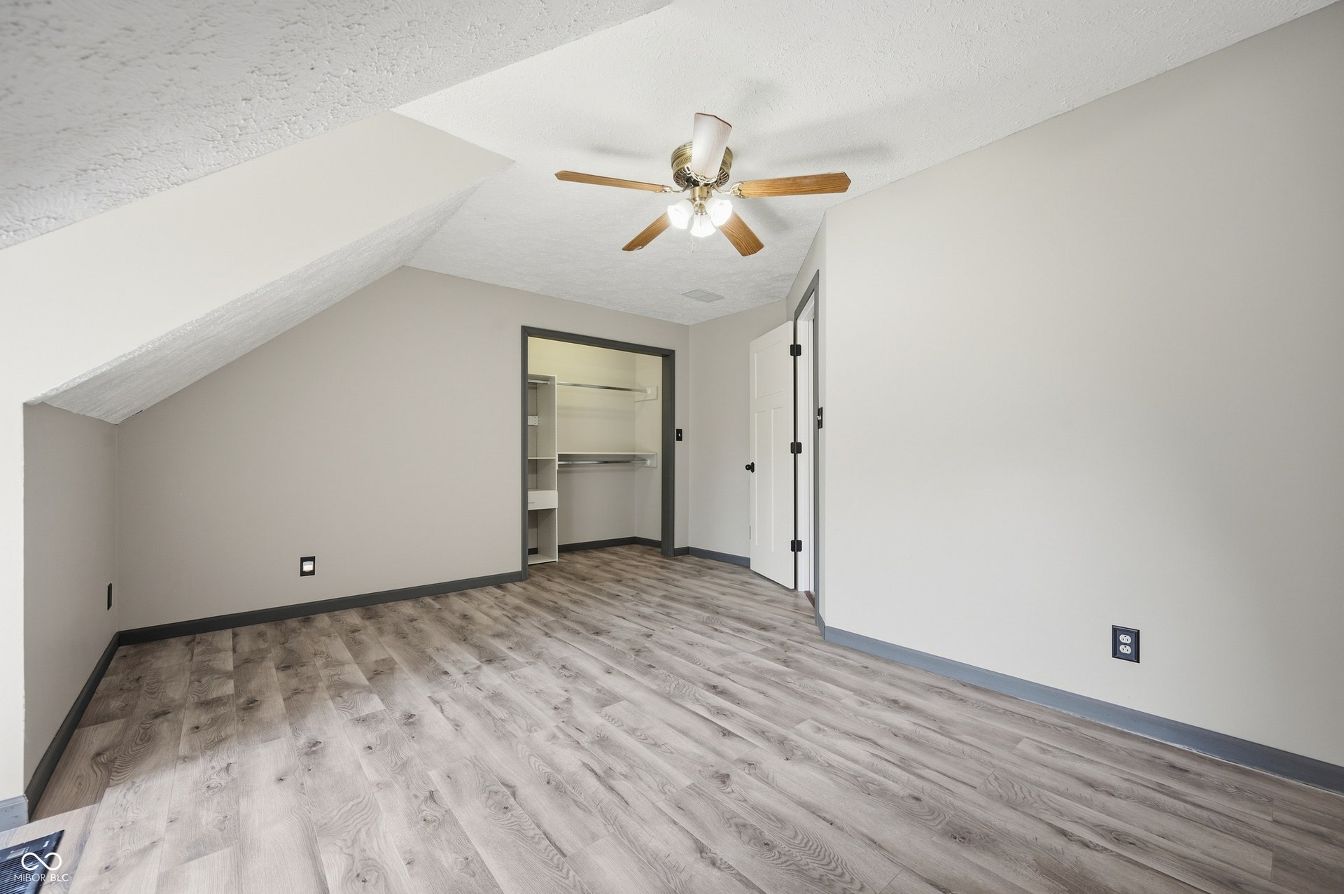 Sloped ceiling lines, wood-finish flooring, ceiling fan, white paneled door, and built-in closet shelving