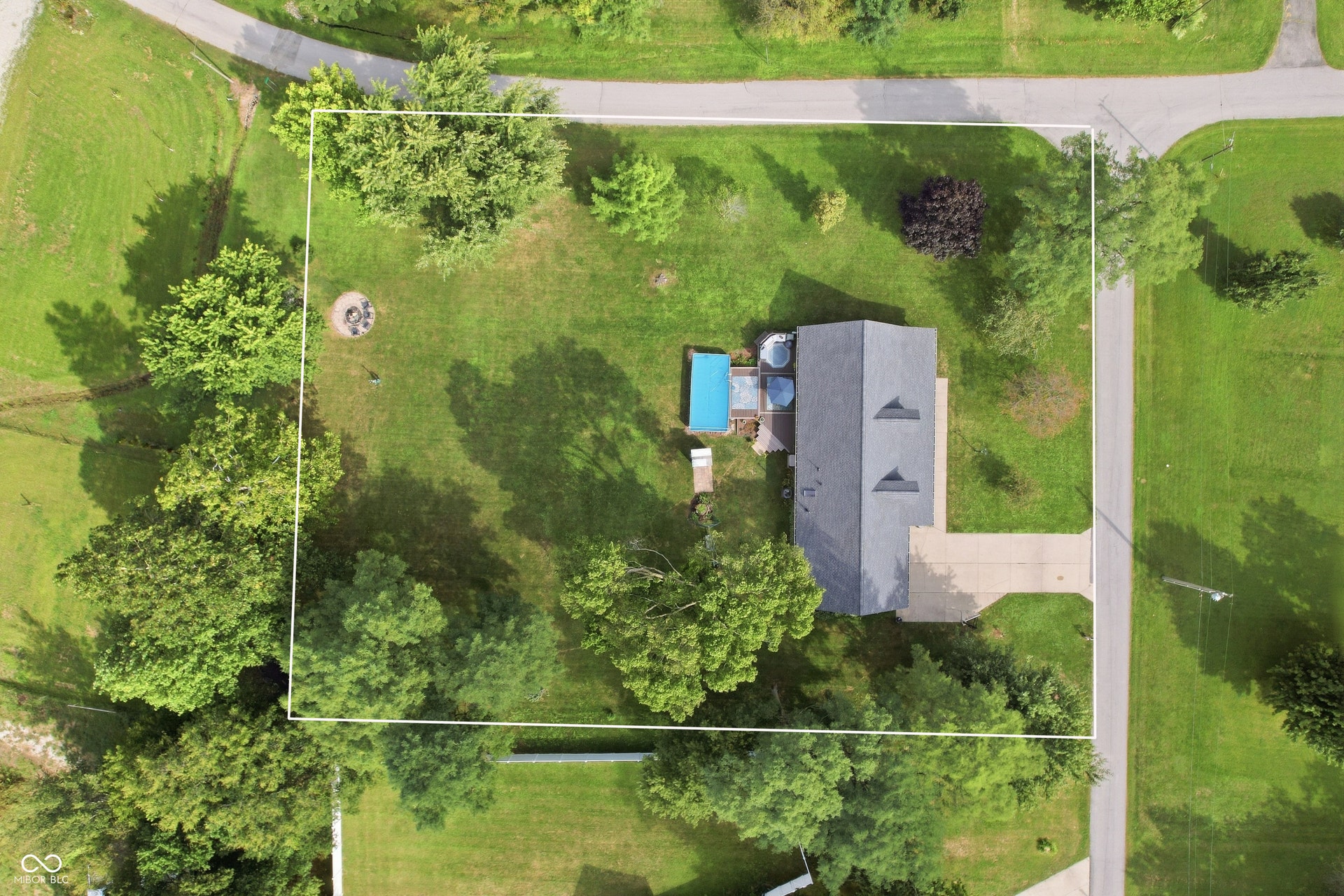 Aerial perspective showcasing a parcel with a residential structure, a paved driveway, and a fire pit