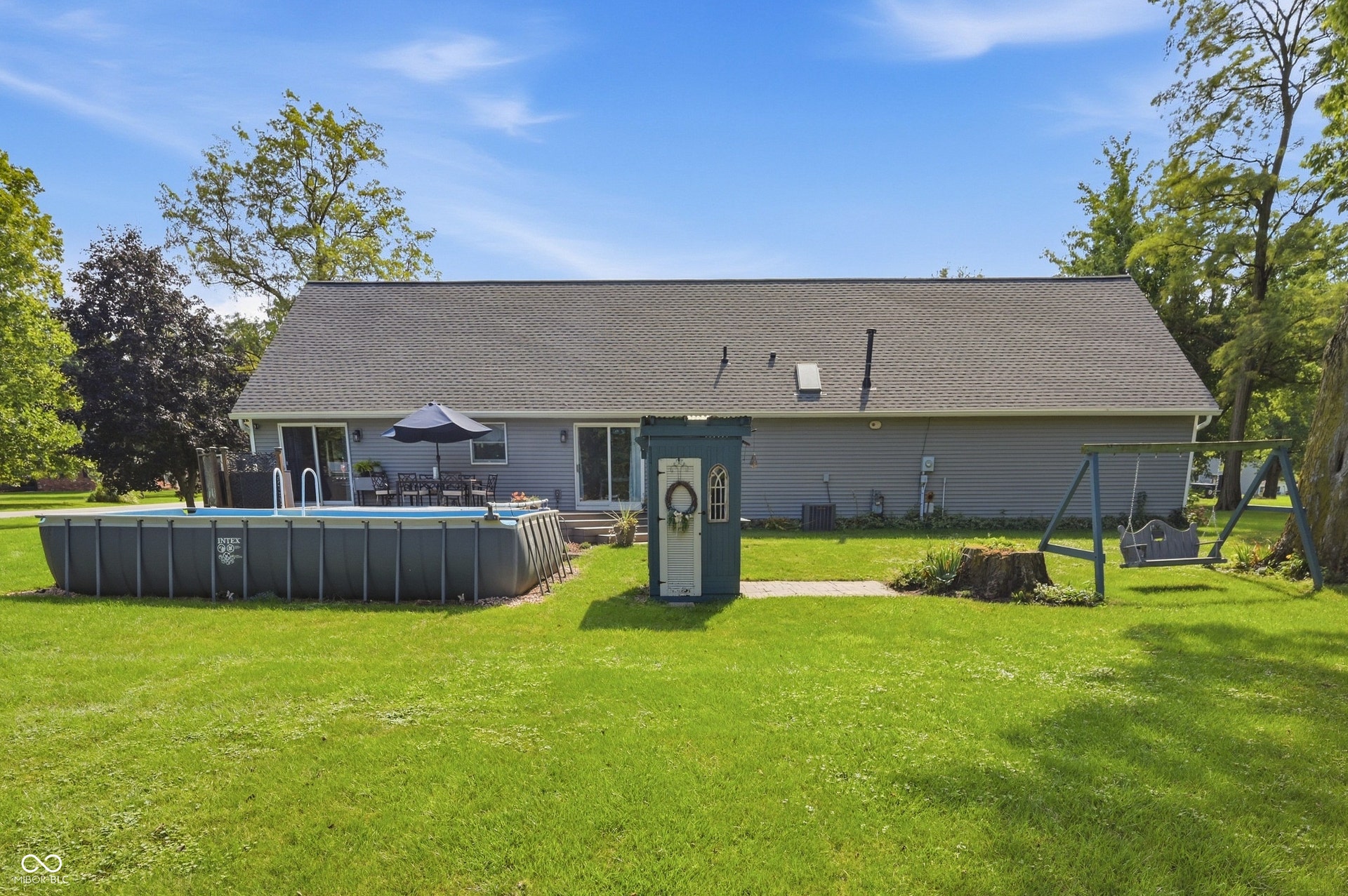 Expansive green lawn with a large above-ground pool, a patio area, and a swing set