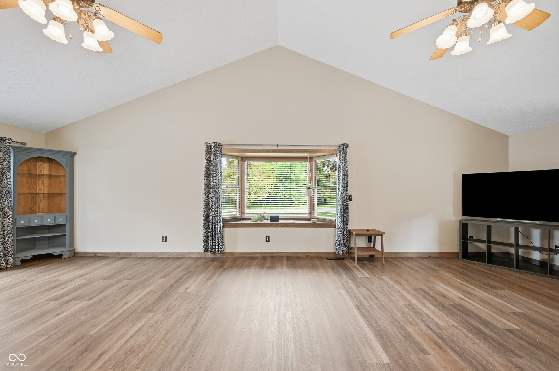 Vaulted ceiling, wood-finish flooring, bay window, two ceiling fans, neutral wall tones