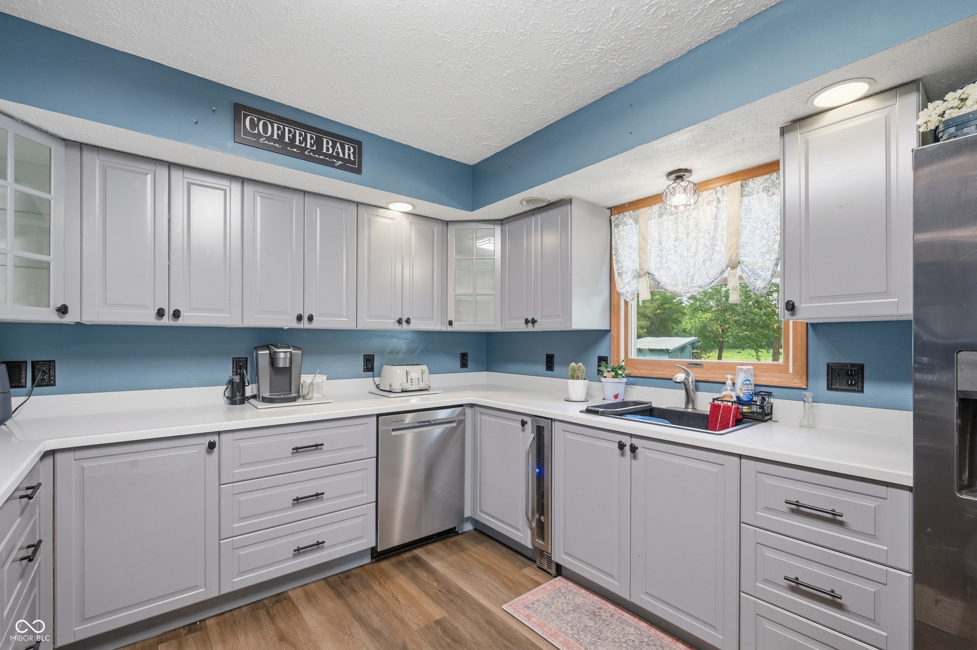 Contemporary kitchen featuring light gray cabinetry, white countertops, stainless steel appliances, wood-finish flooring, and a window with a wood frame
