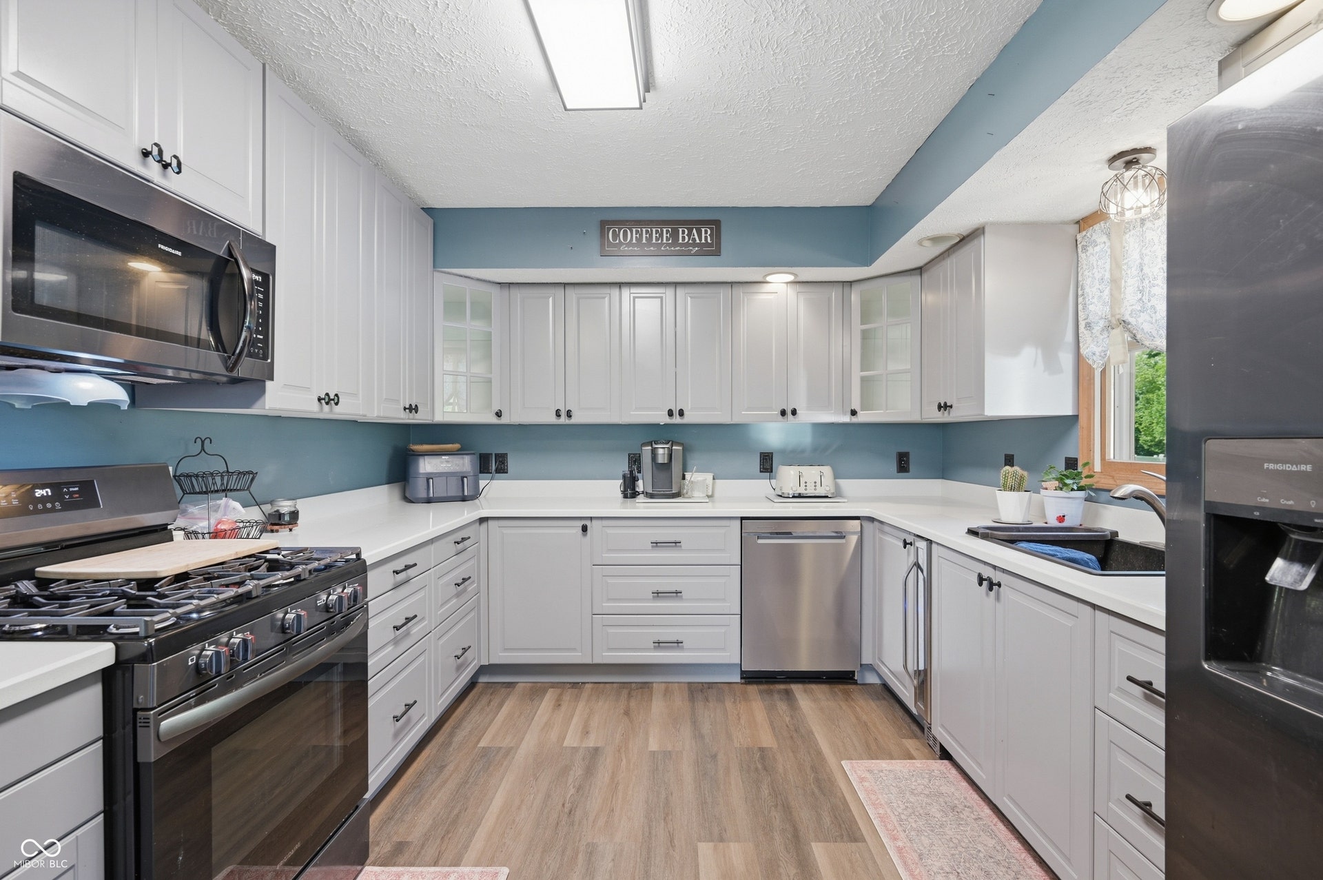 U-shaped kitchen featuring wood-finish flooring, light gray cabinetry with dark hardware, white countertops, and stainless steel appliances