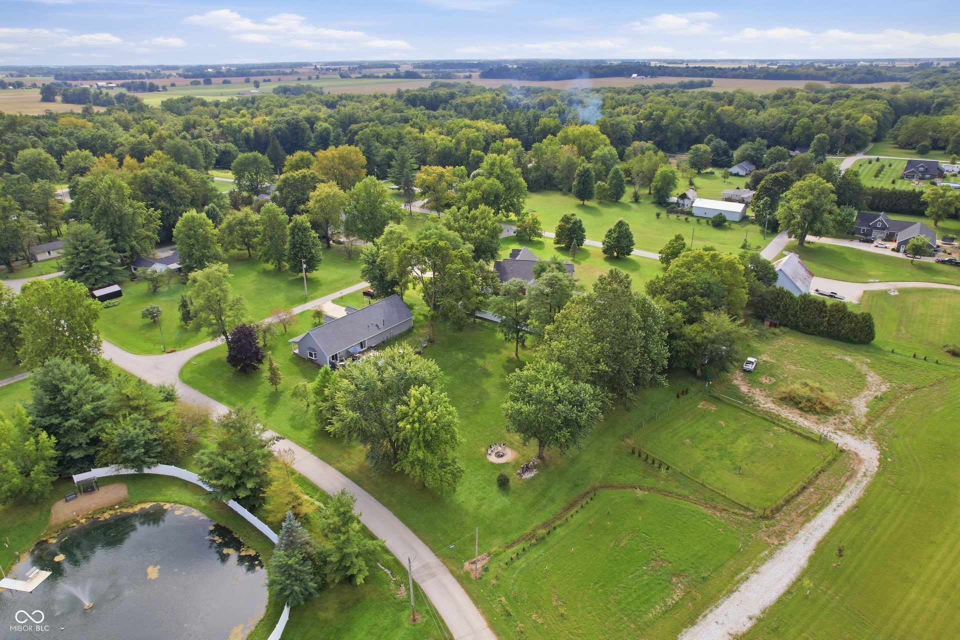 Expansive property featuring a private pond with a fountain, mature trees, substantial green space, and a gravel driveway