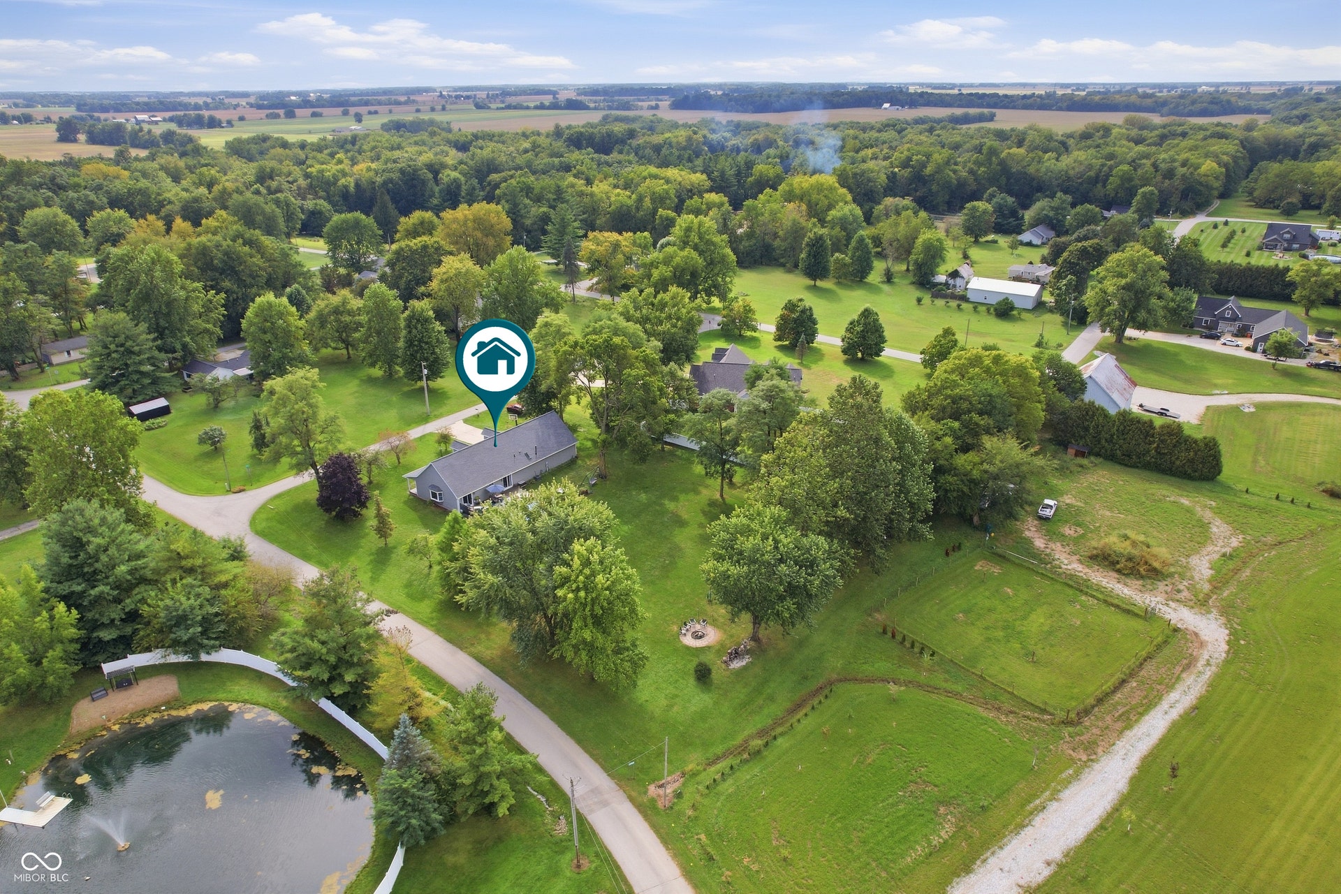 Aerial perspective showcasing the property's expansive grounds, surrounding mature trees, and a private pond with a fountain feature