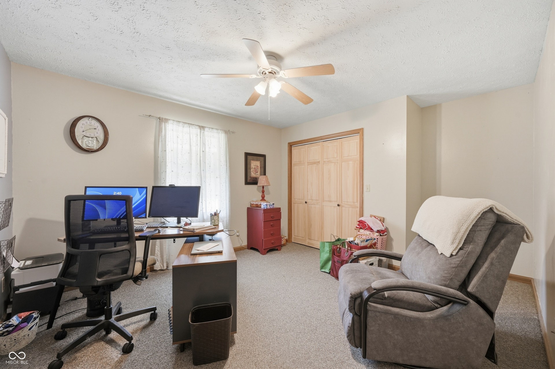 Carpeted room featuring a ceiling fan, window with sheer curtains, bi-fold closet doors, and light-toned walls