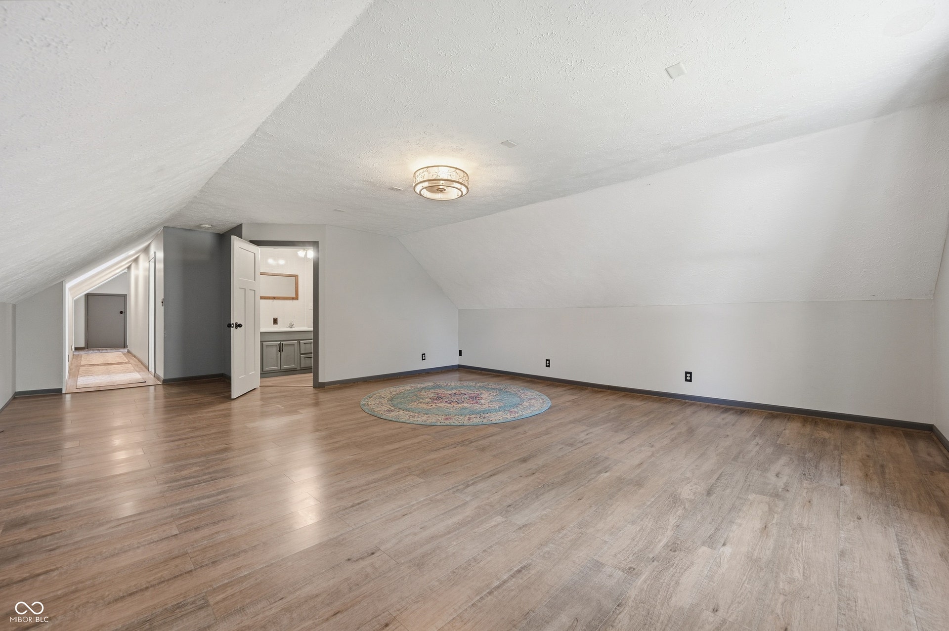 Sloped ceilings, wood-finish flooring, and a contemporary ceiling light fixture