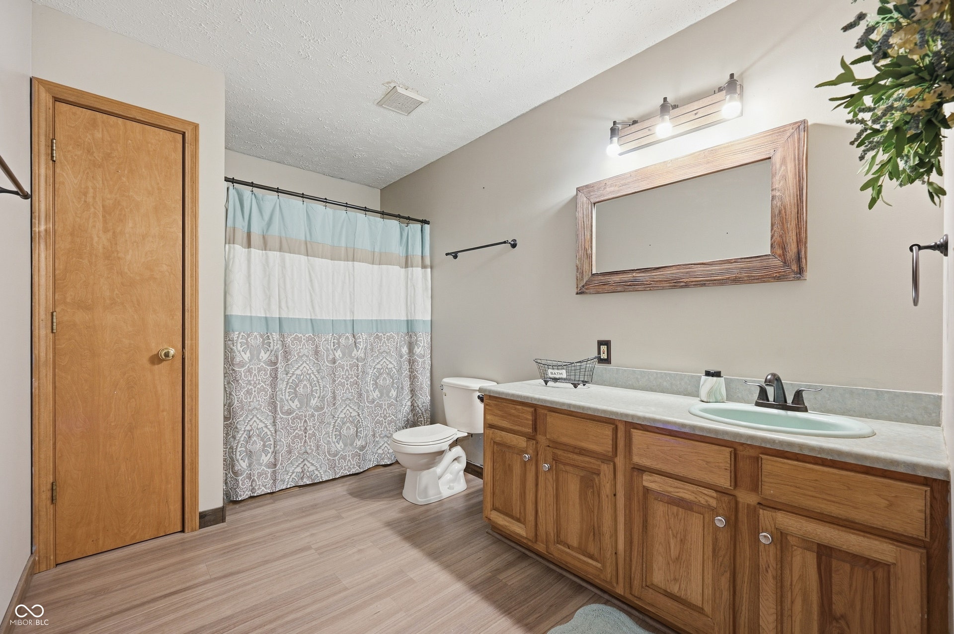 Wood-finish flooring, single vanity with wood cabinetry, rectangular mirror with wood frame, and overhead vanity lighting