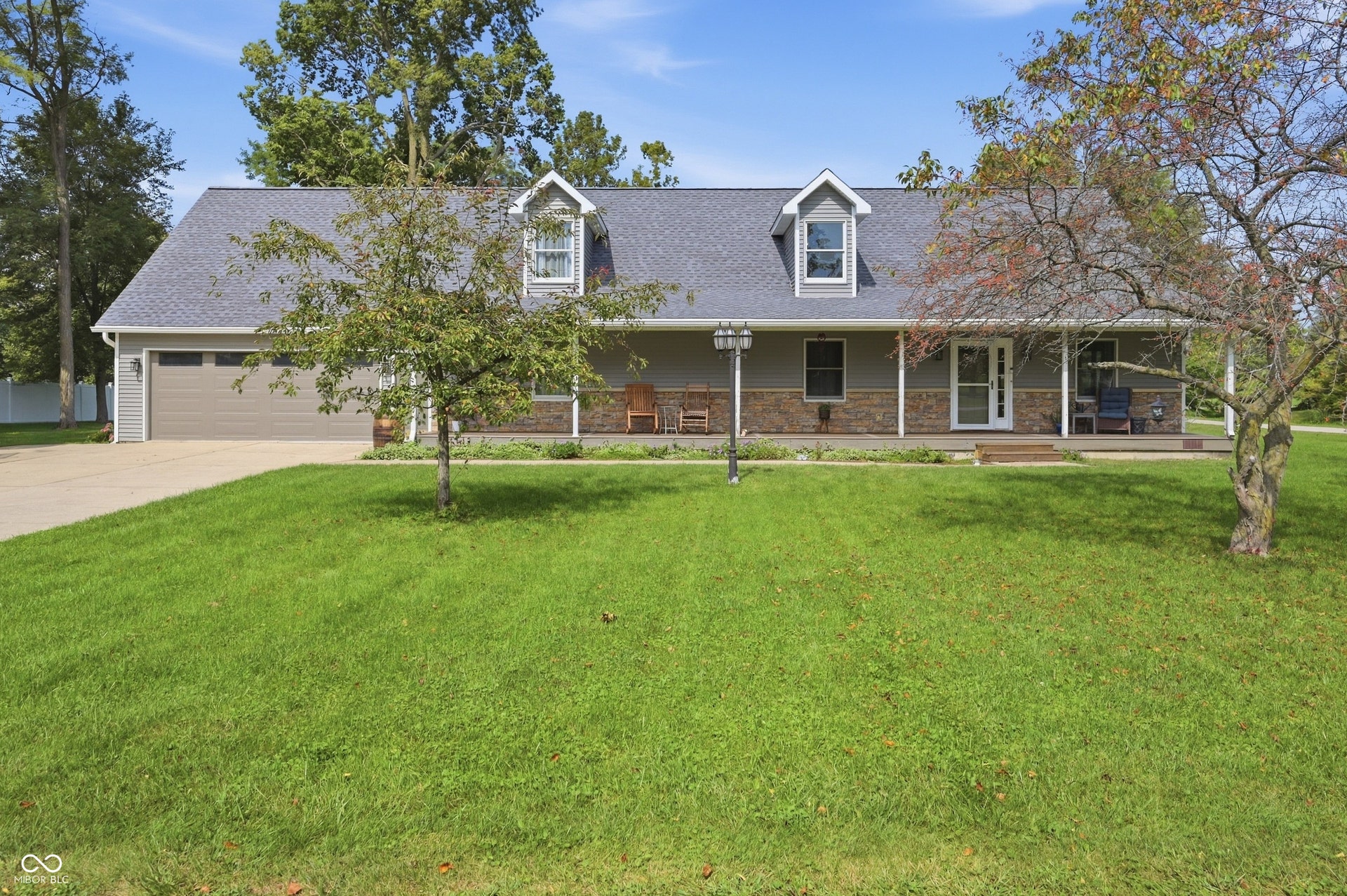 Ranch-style residence featuring a covered front porch, stone and siding exterior, and a two-car garage