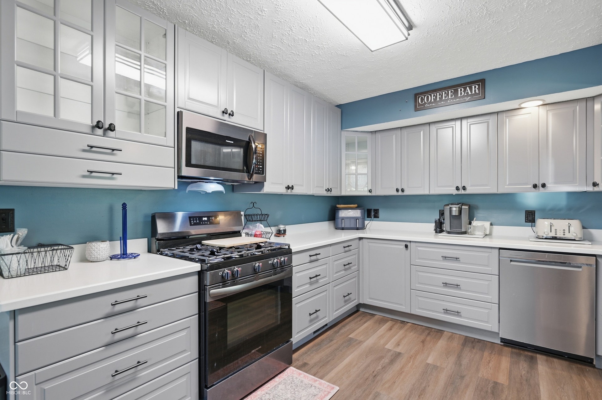 Corner kitchen featuring light gray cabinetry, stainless steel appliances, white countertops, and wood-finish flooring
