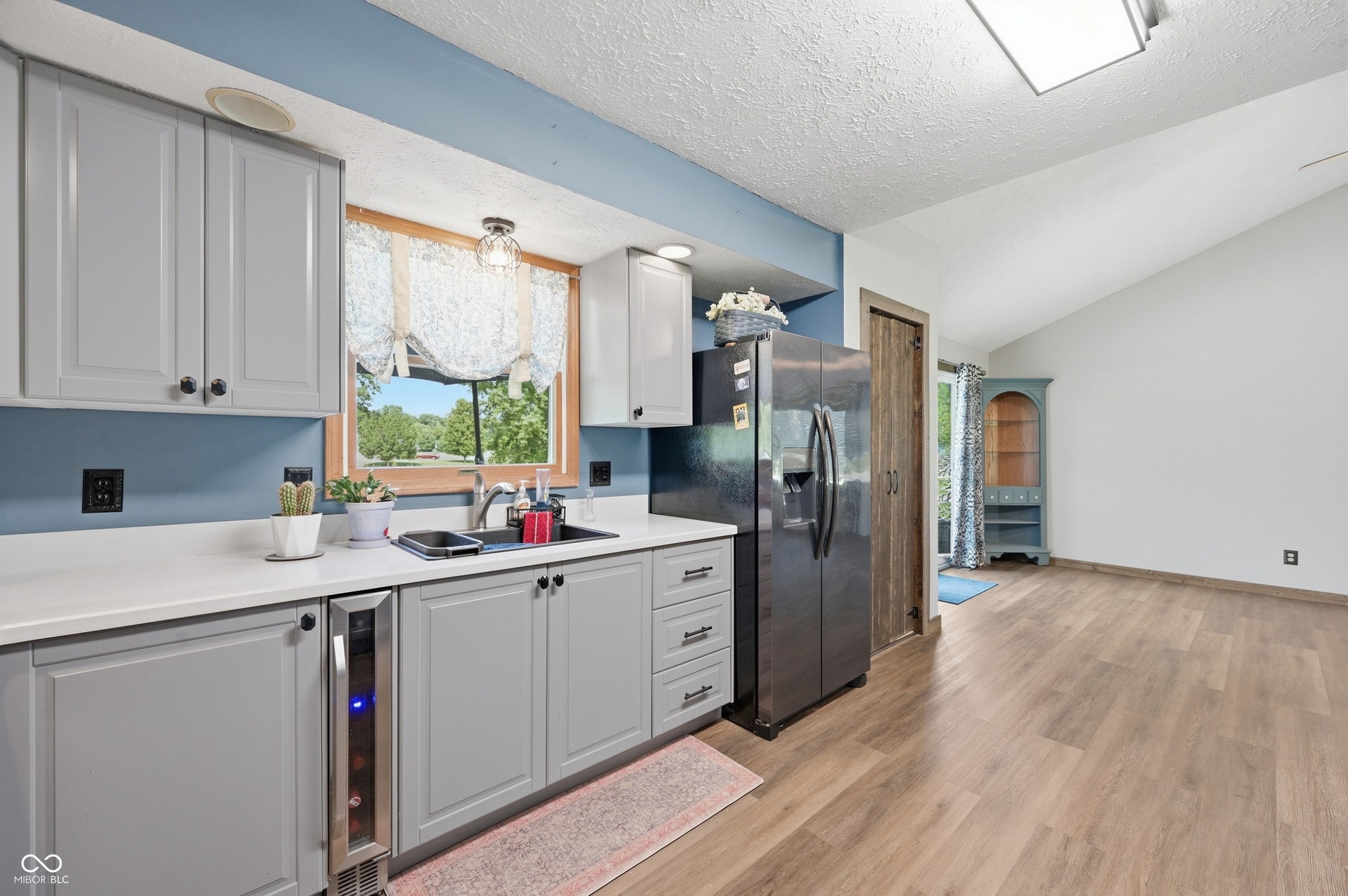 Kitchen featuring gray cabinetry, white countertops, wood-finish flooring, a built-in wine cooler, and a vaulted ceiling