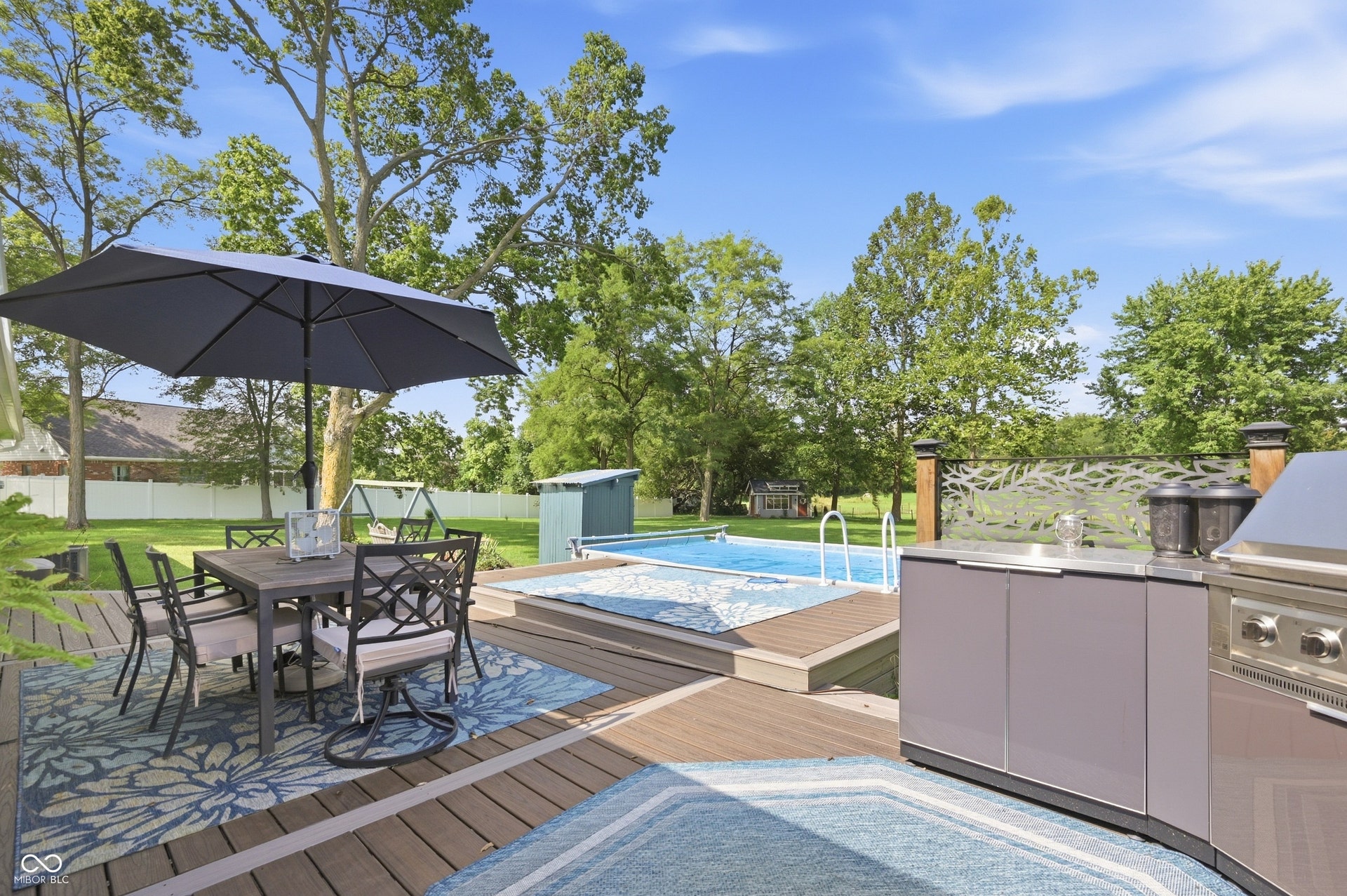 Expansive outdoor deck with a built-in outdoor kitchen, an in-ground swimming pool, and a decorative privacy screen