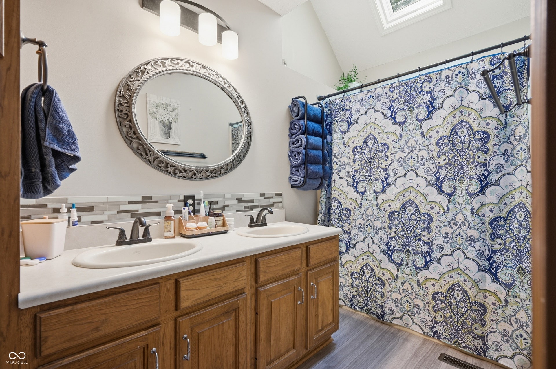 Dual vanity with white countertops, wood-finish cabinetry, and a mosaic tile backsplash