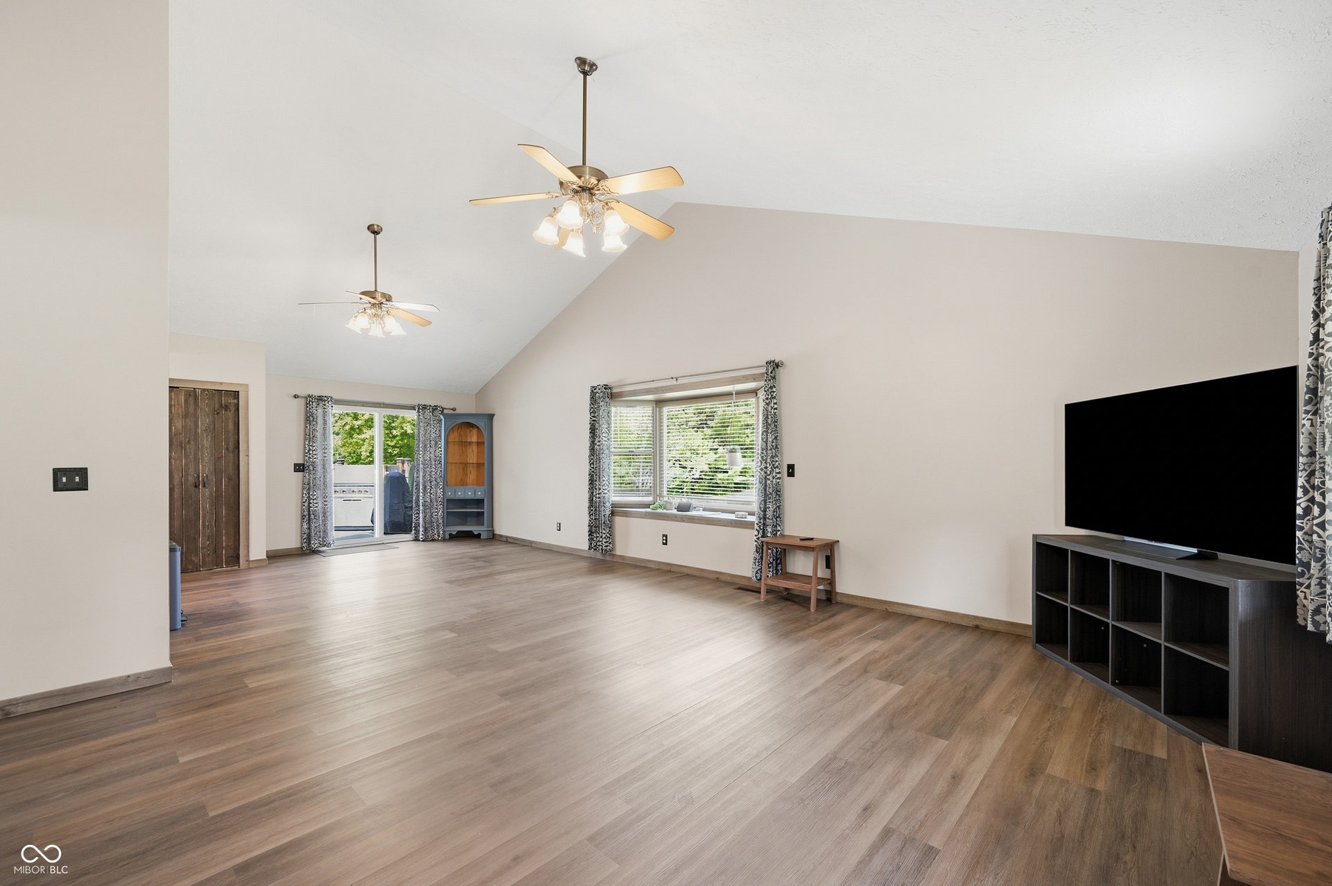 Vaulted ceiling with dual ceiling fans, wood-finish flooring, large bay window, and glass sliding door