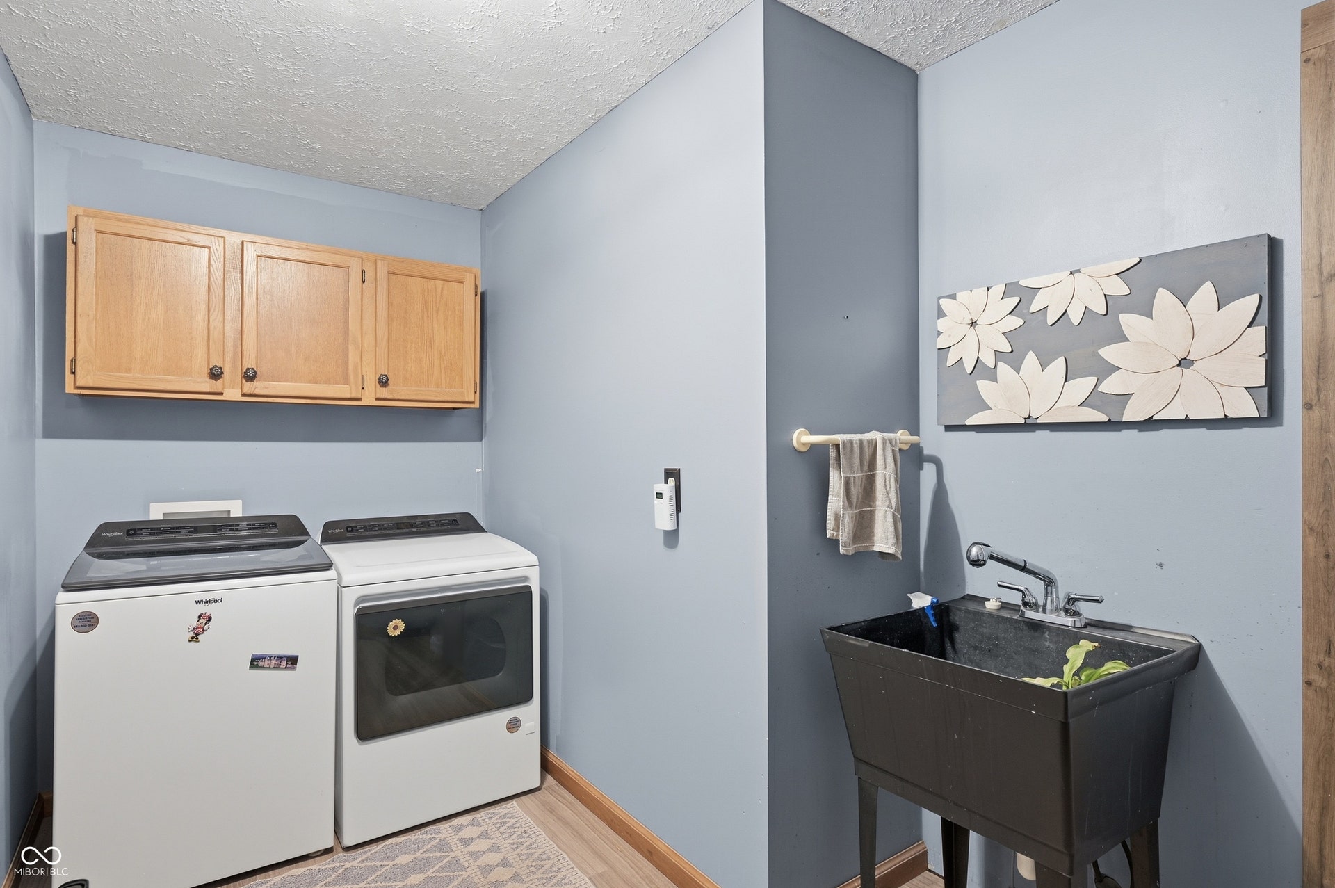 Laundry area featuring wood-finish flooring, overhead cabinetry, and a utility sink