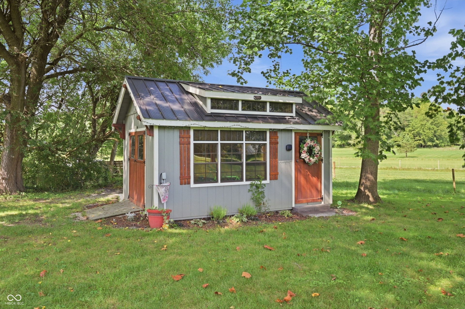 Detached outbuilding with a gabled roof, metal roof, transom windows, and wood shutters