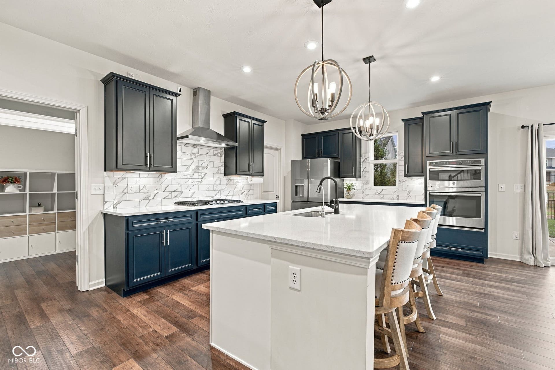 Luxury Kitchen with large island and seating w/ fwood-finish flooring, dark blue cabinetry, white countertops, and stainless steel appliances