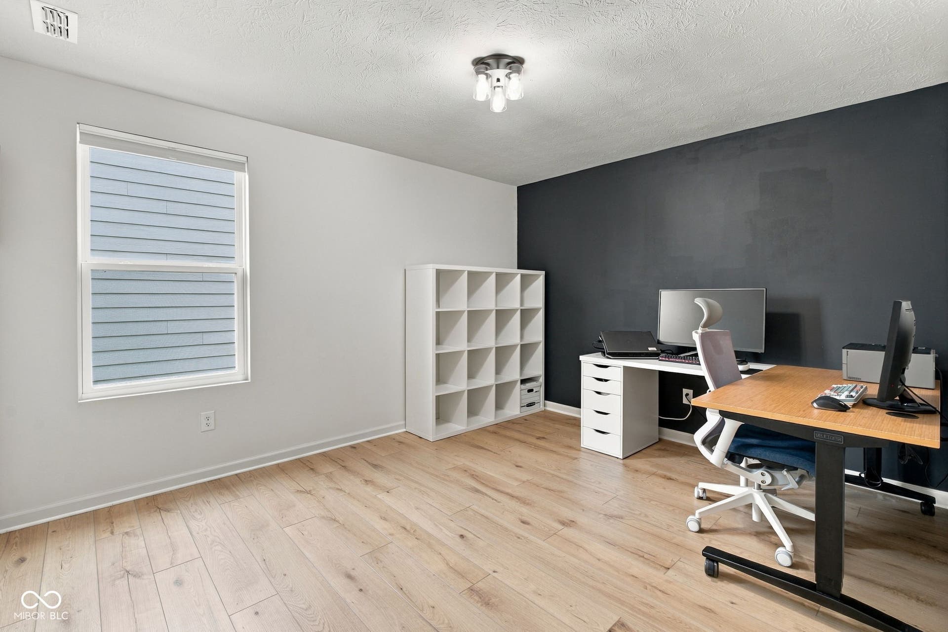 Light wood-finish flooring complemented by a contrasting accent wall, a single window, and a flush-mount ceiling fixture