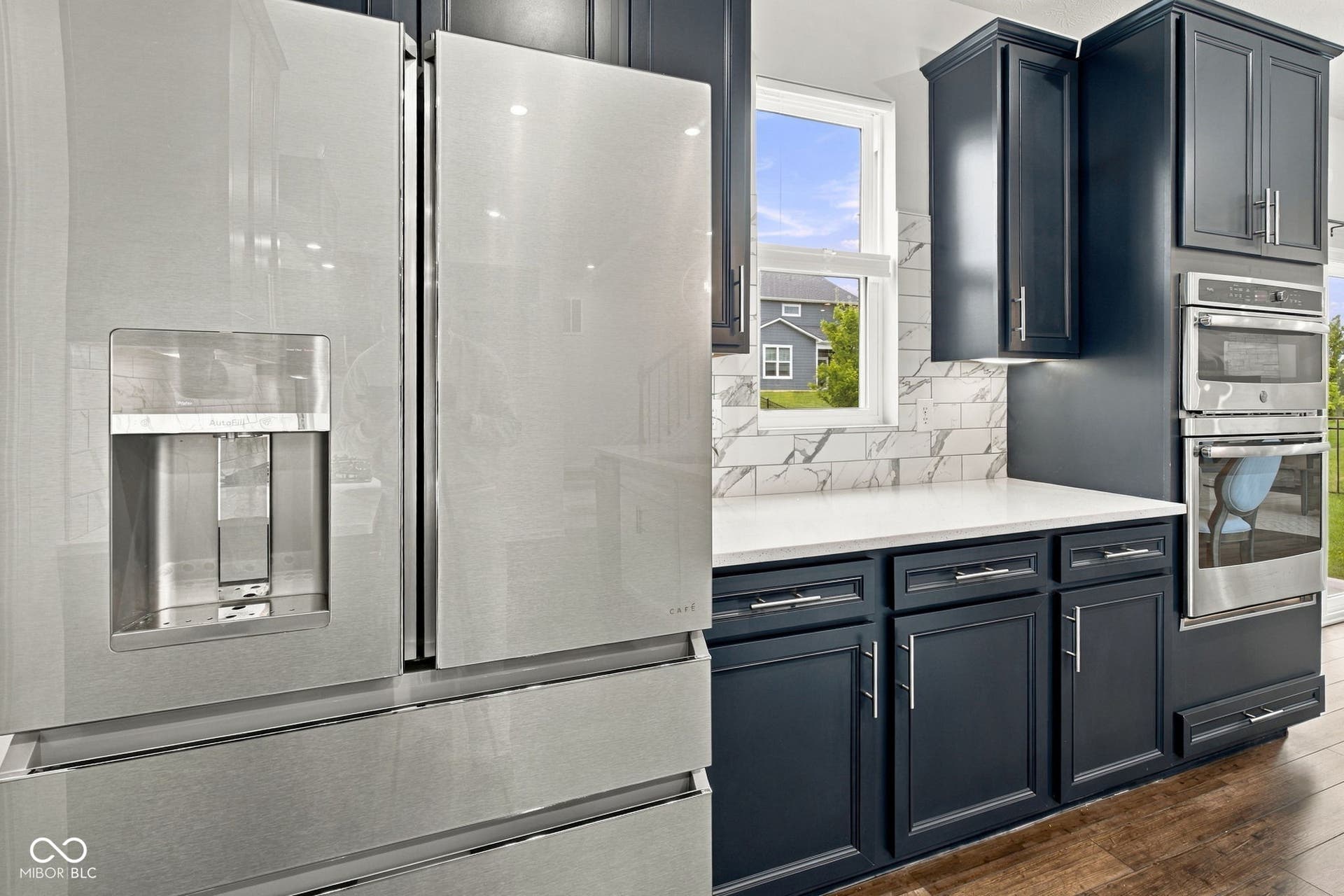 Stainless steel refrigerator, cabinetry w/ hardware, built-in stainless steel oven, white countertops, and a white tiled backsplash