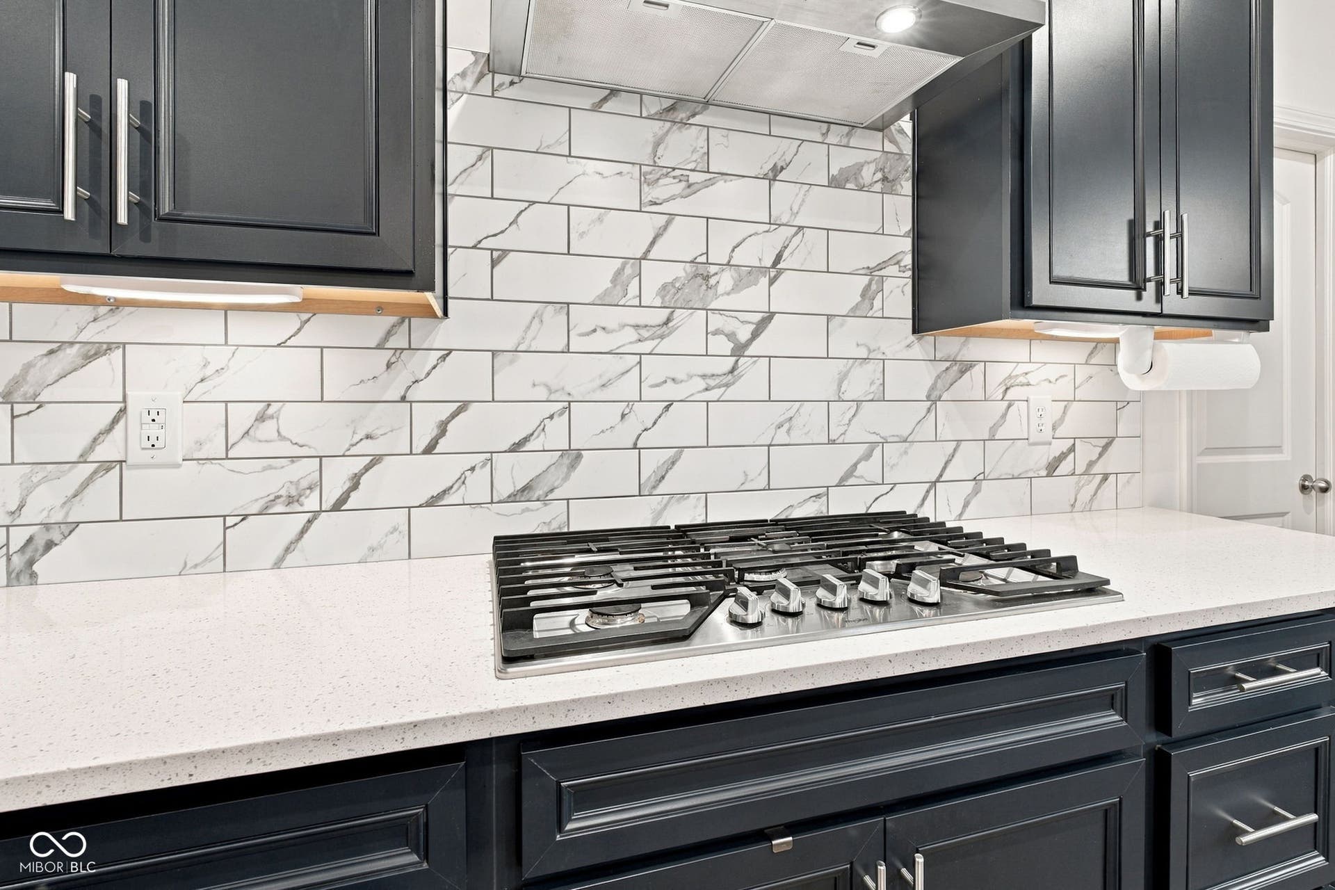 Stainless steel gas range with a tile backsplash, cabinetry, light countertops, and a stainless steel range hood
