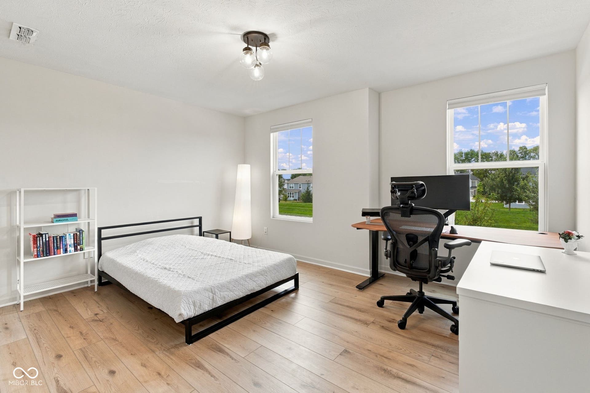 Light wood-finish flooring, white painted walls, two large windows, and a multi-bulb ceiling light fixture