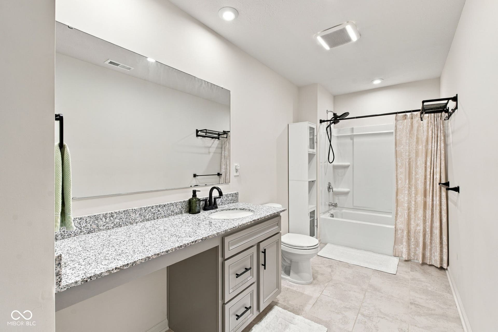 Spacious bathroom featuring a single vanity with stone-finish countertop, undermount sink, and dark-finish hardware