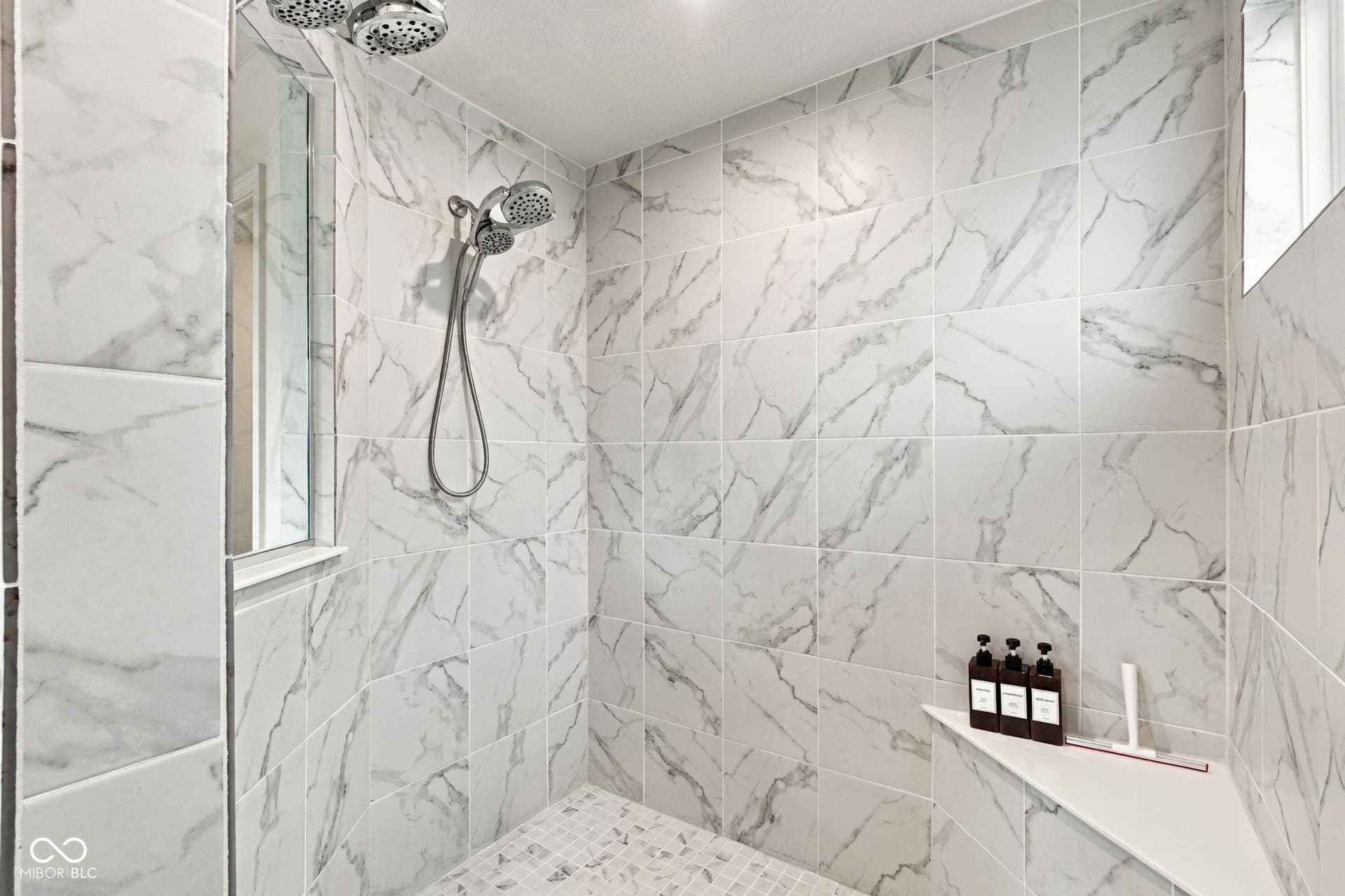 Tiled shower with a dual shower head system, integrated shelving, and a mosaic tile floor