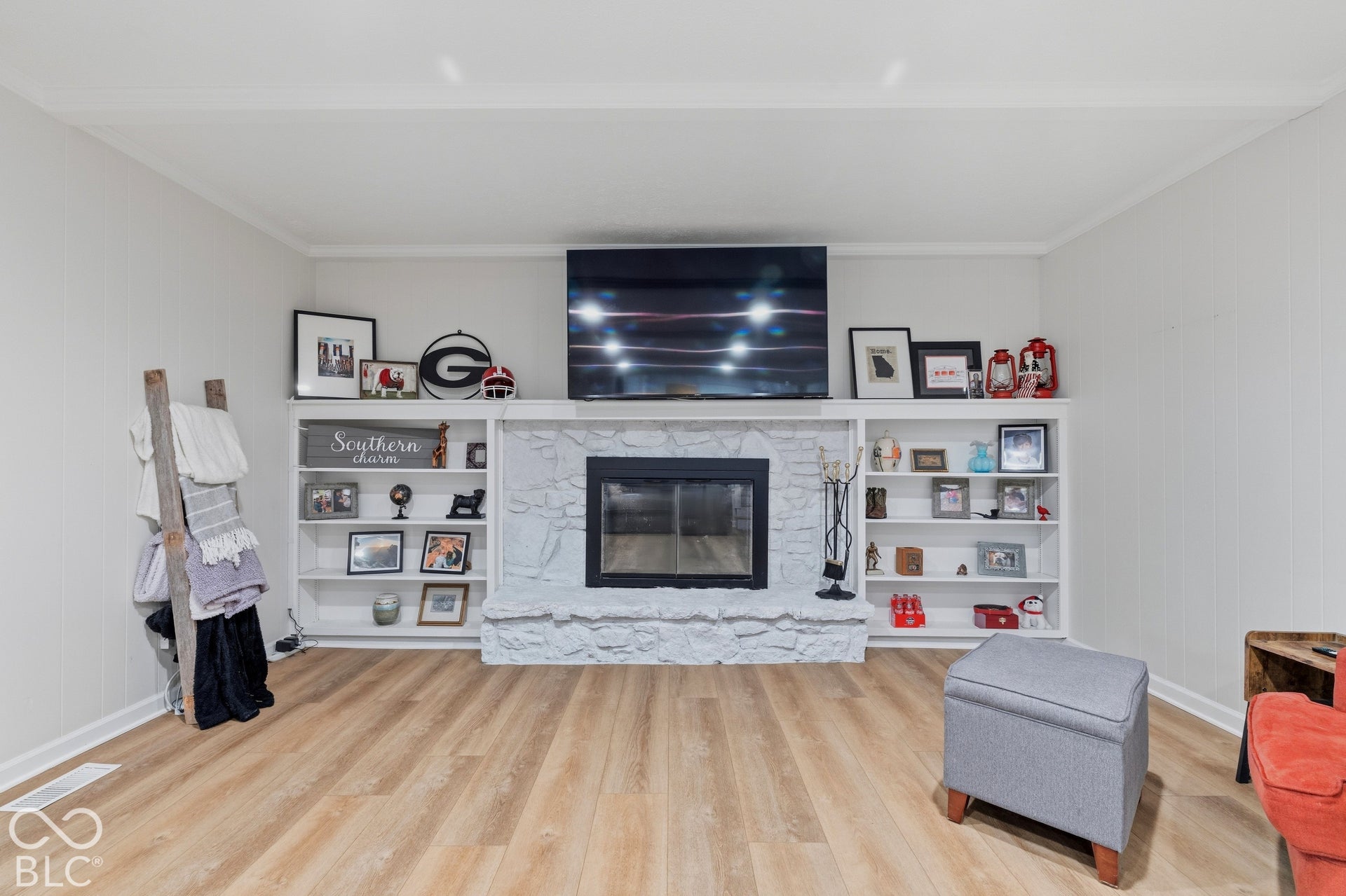 White-painted stone fireplace with hearth, integrated built-in shelving, crown molding, and wood-finish flooring